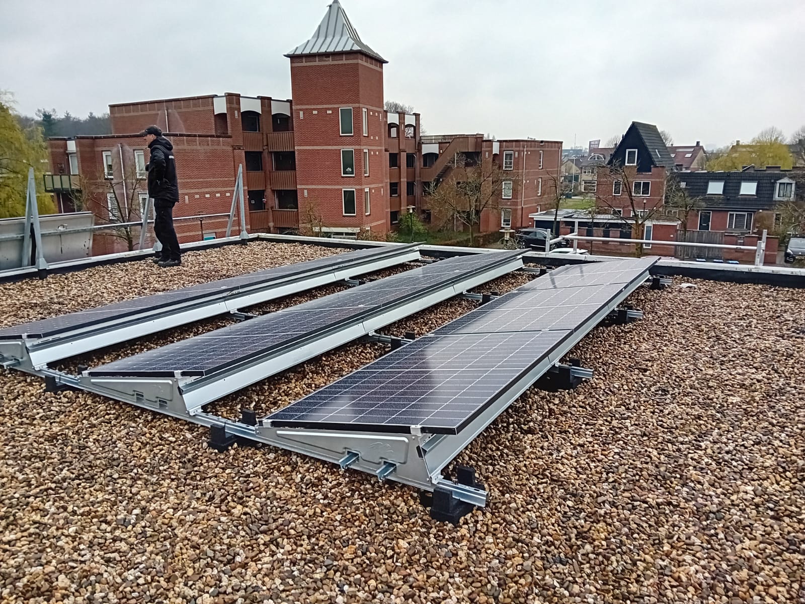 De foto toont zonnepanelen geïnstalleerd op een dak met grindbedekking. Een technicus is bezig met de installatie.