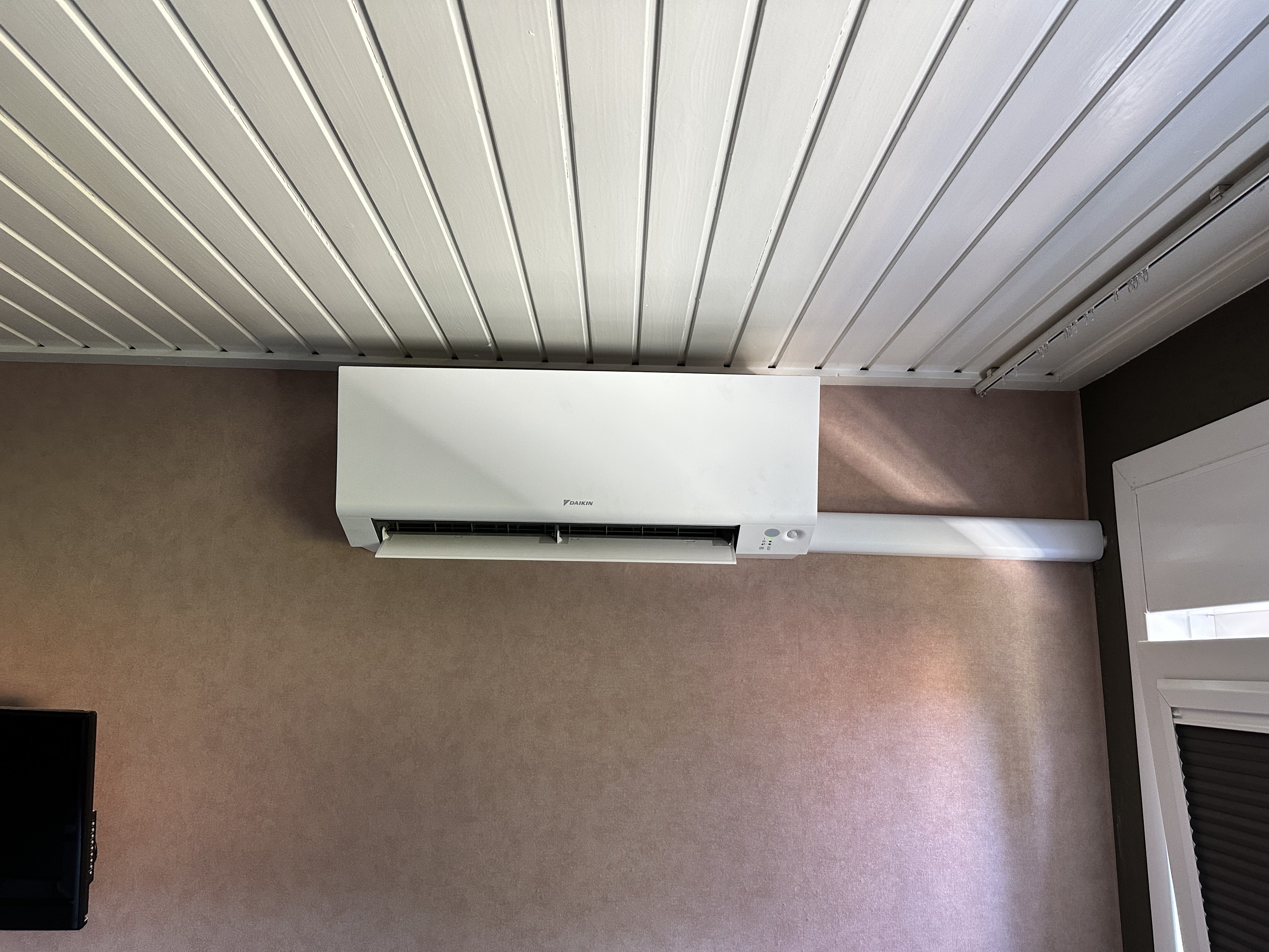 Moderne wand-airco-unit geïnstalleerd tegen een lichtgekleurde muur, met zichtbare leidingen.