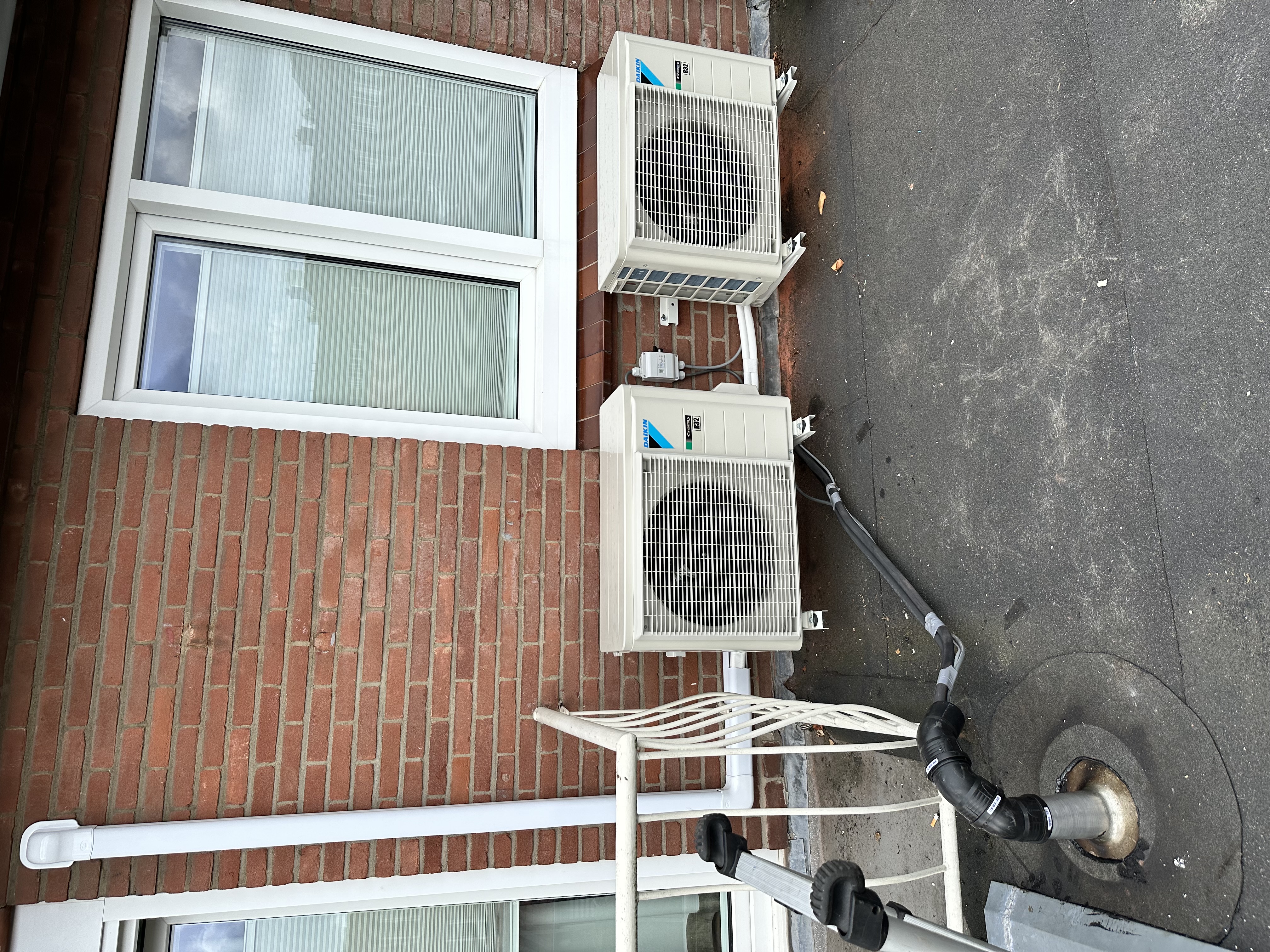 Deze afbeelding toont een buitenunit van een airconditioningsysteem, geplaatst tegen een bakstenen muur.