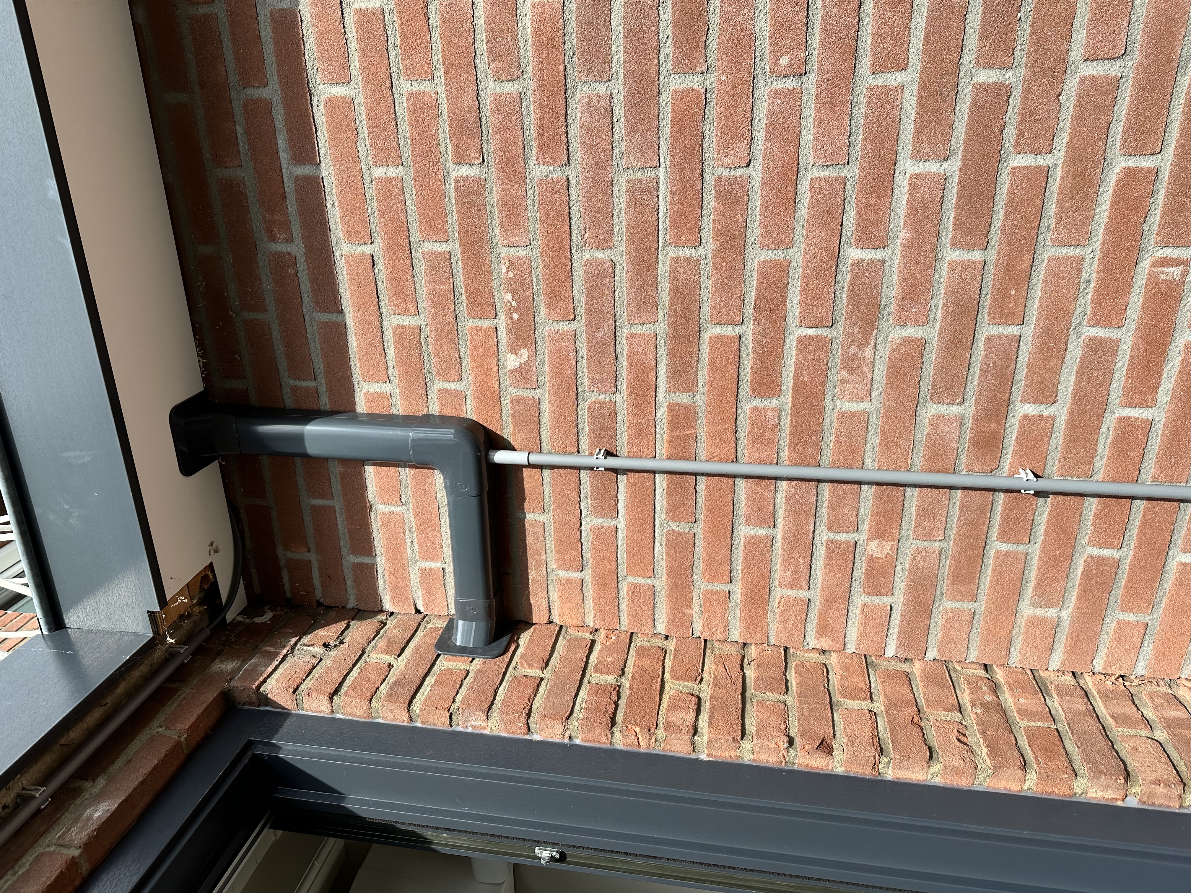De installatie toont een afvoerpijp voor een airconditioningseenheid die aan de wand is bevestigd.