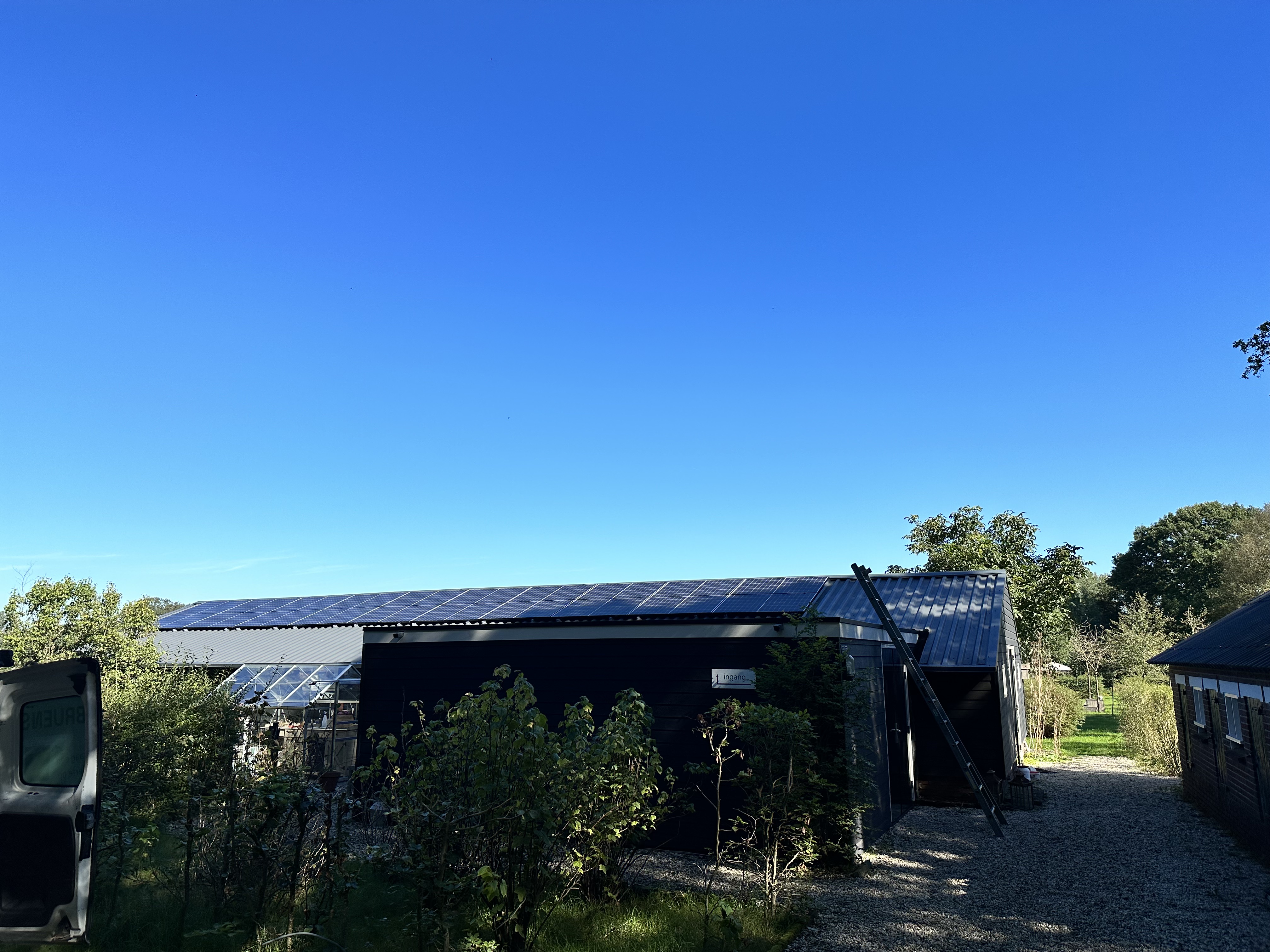Deze afbeelding toont een woning met zonnepanelen op het dak, omringd door groen en een heldere blauwe lucht.