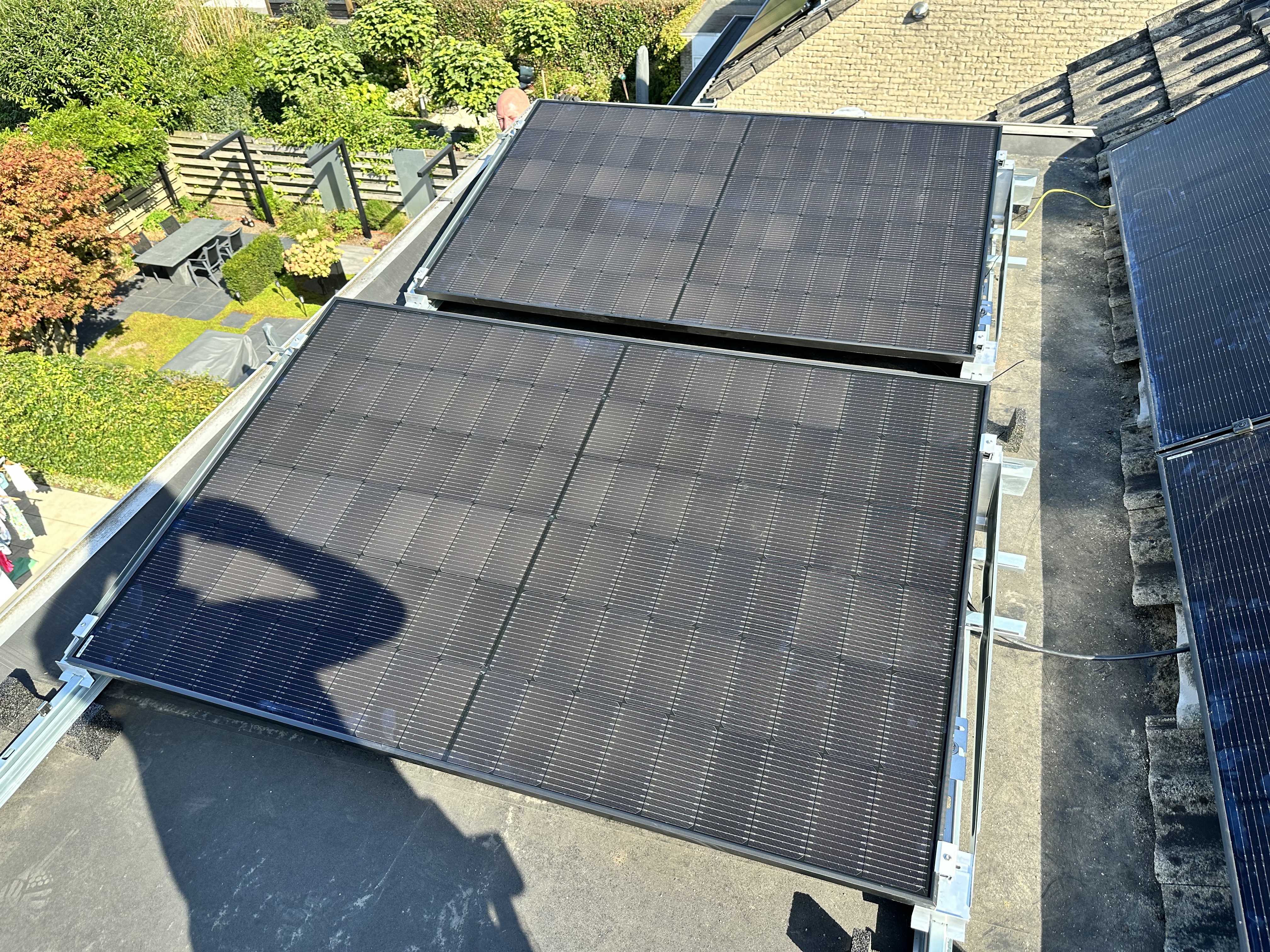 Twee zonnepanelen zijn geïnstalleerd op een schuin dak, met een uitzicht op een groene tuin.