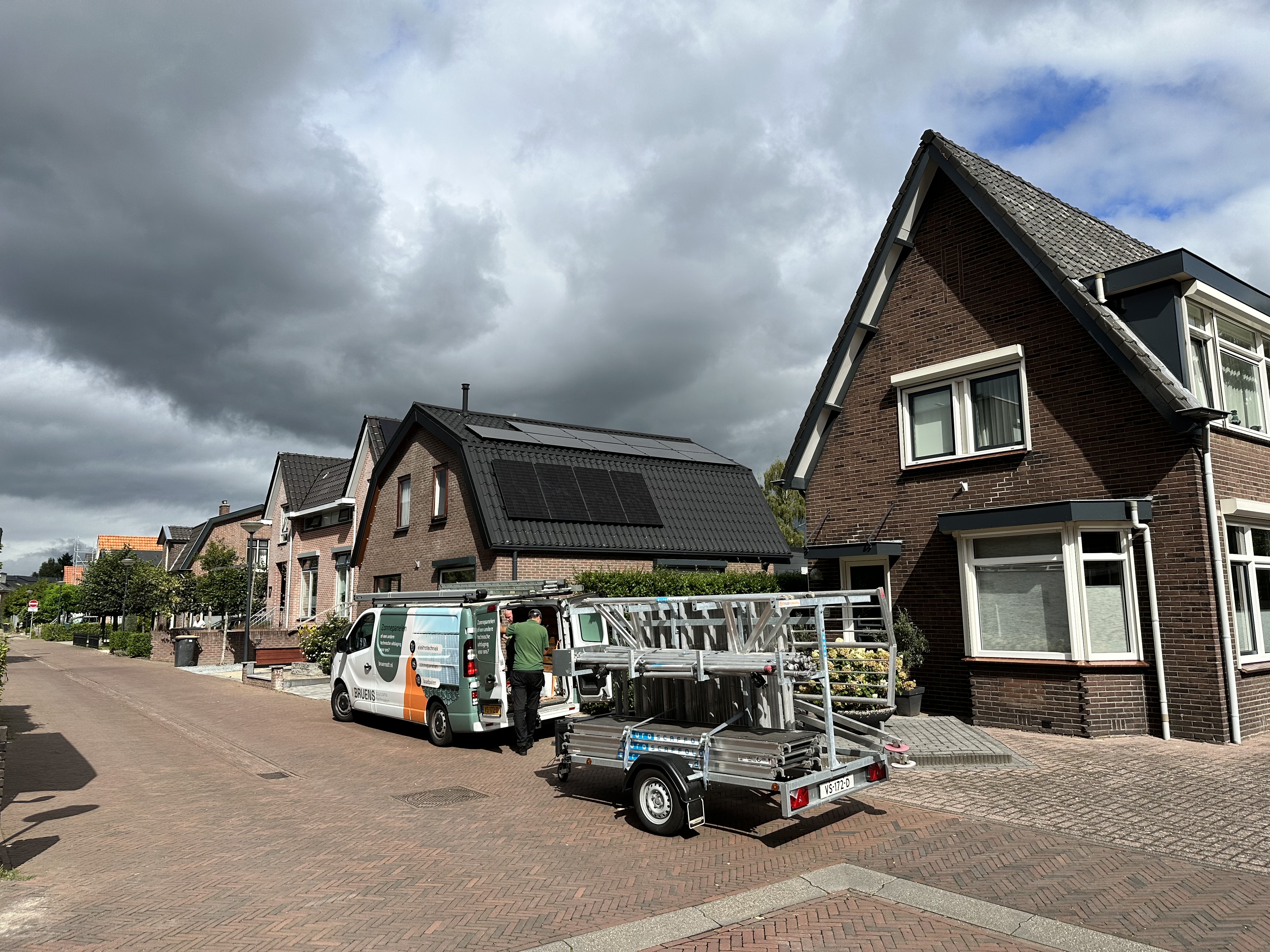 De afbeelding toont een woning met zonnepanelen op het dak, waar een installatieploeg aan het werk is.