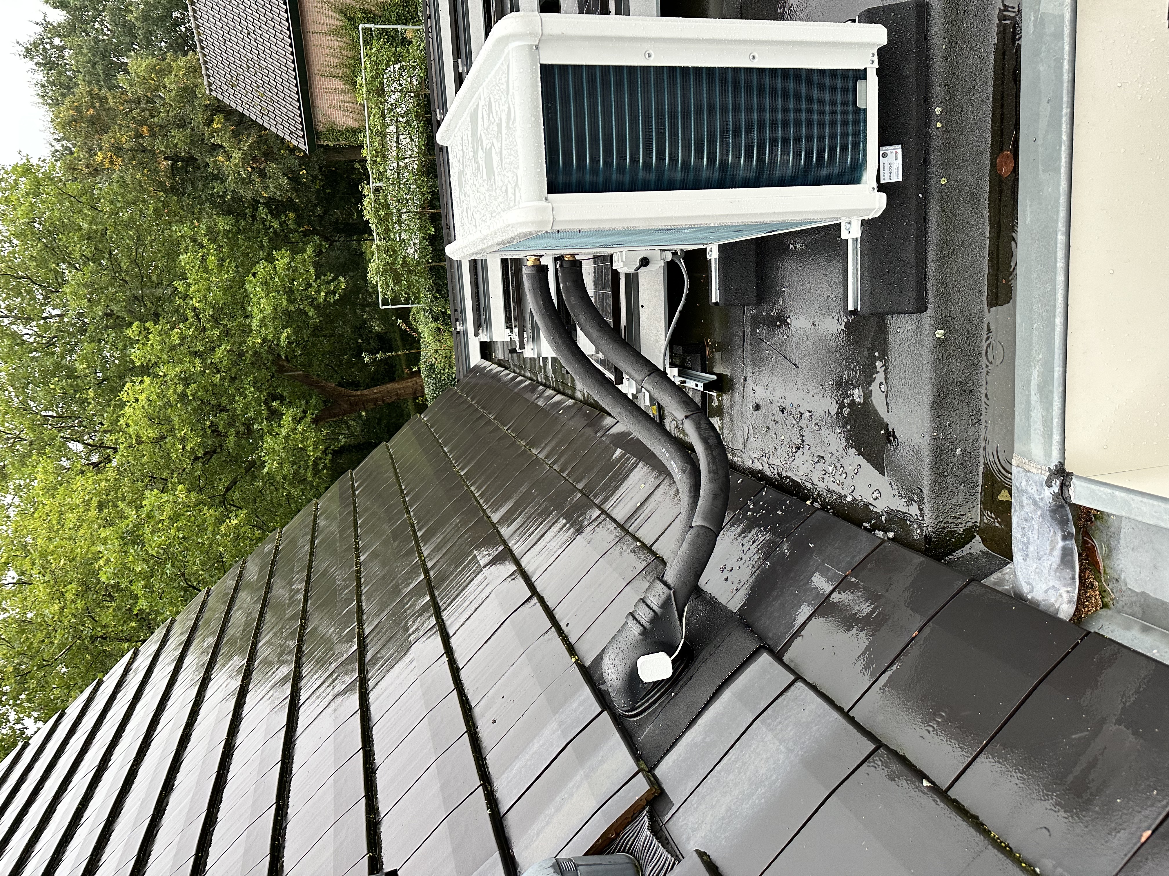 De foto toont een airconditioningunit geïnstalleerd op een dak met gebruikelijke afvoerslangen en een modern ontwerp.