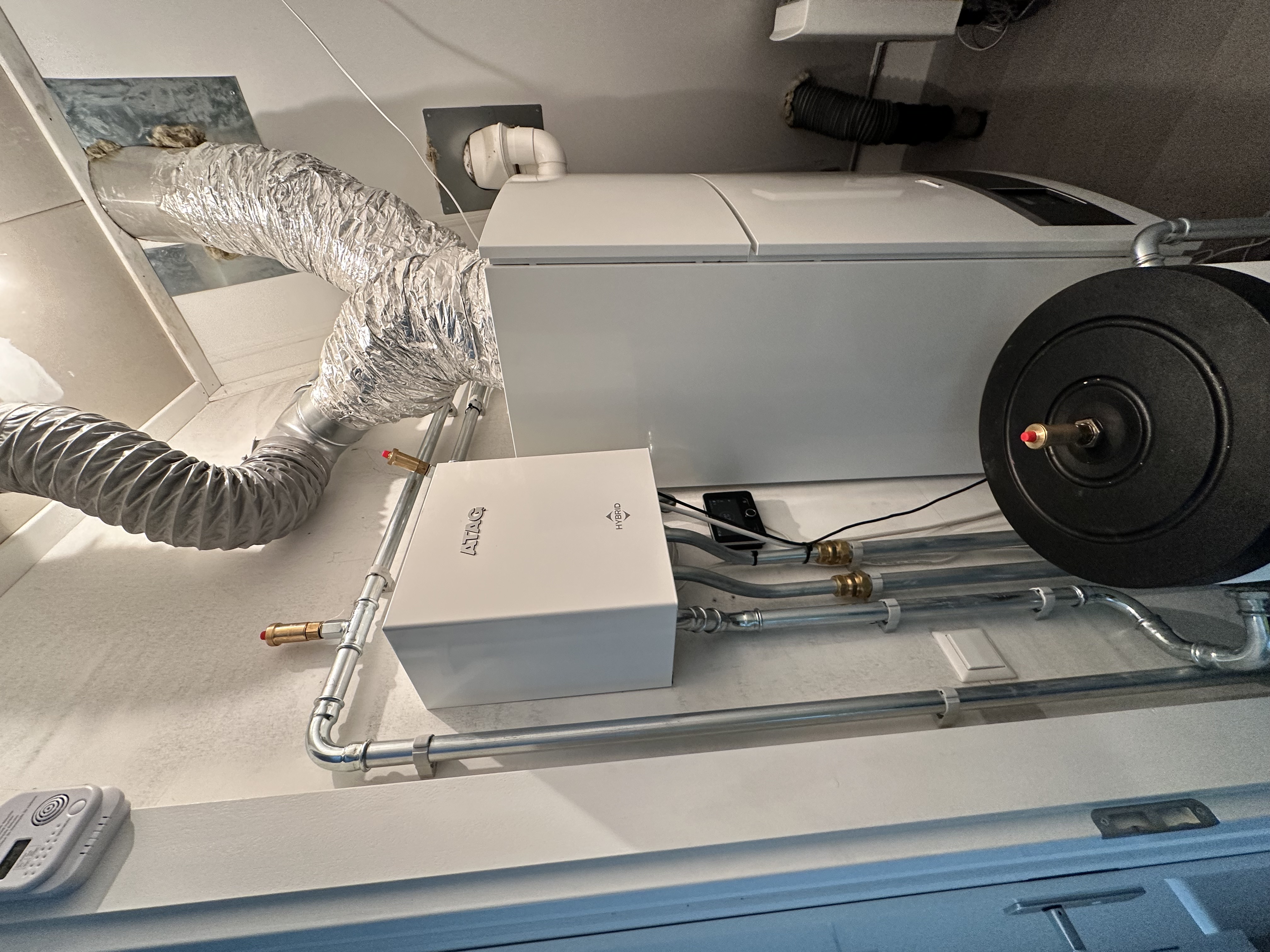 De installatie toont een warmtepomp met leidingen en een opslagtank, die samen zorgen voor verwarmingsoplossingen in een woning.