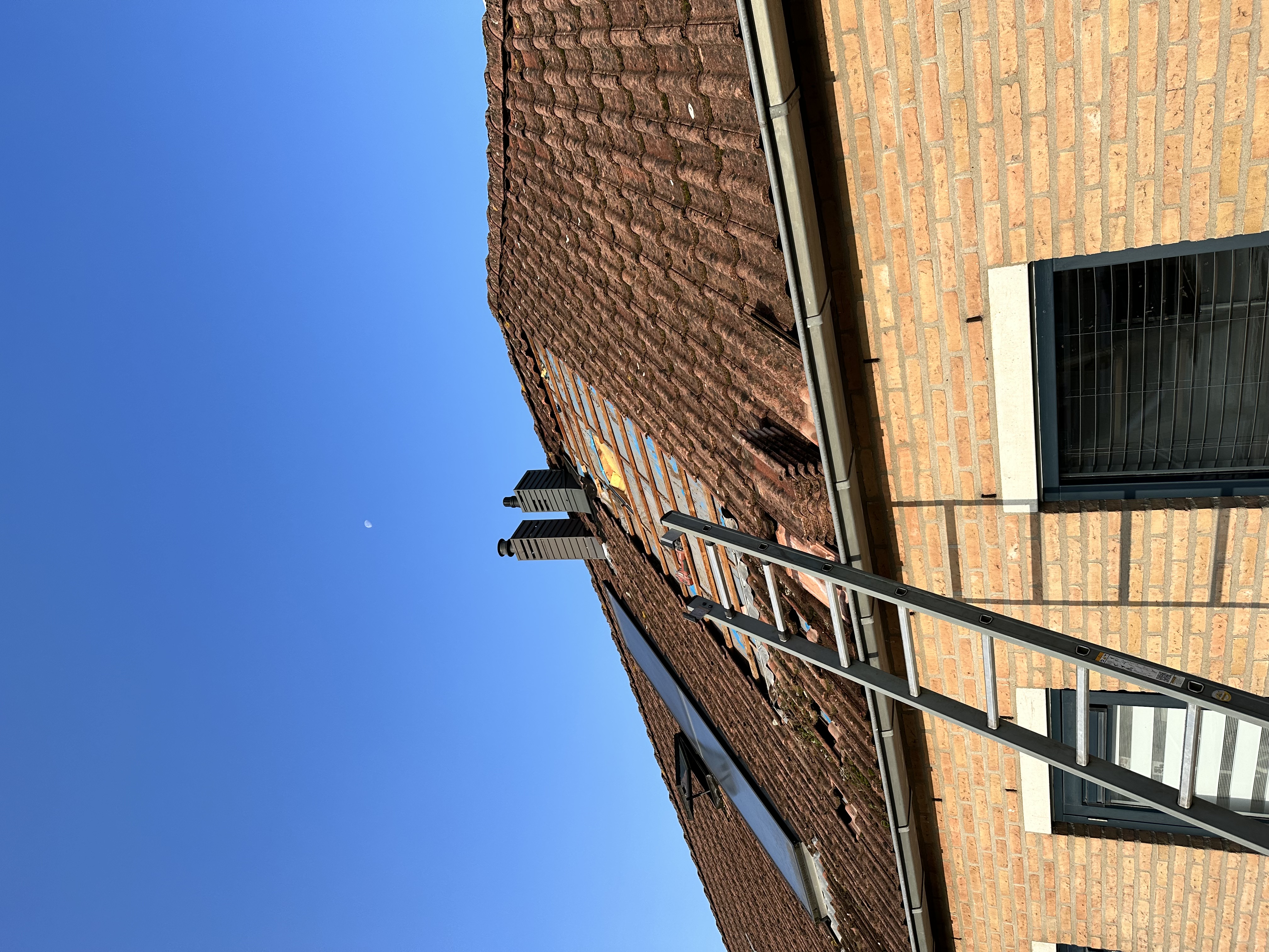 De foto toont een dak waar zonnepanelen worden geïnstalleerd, met een ladder die naar het dak leidt.