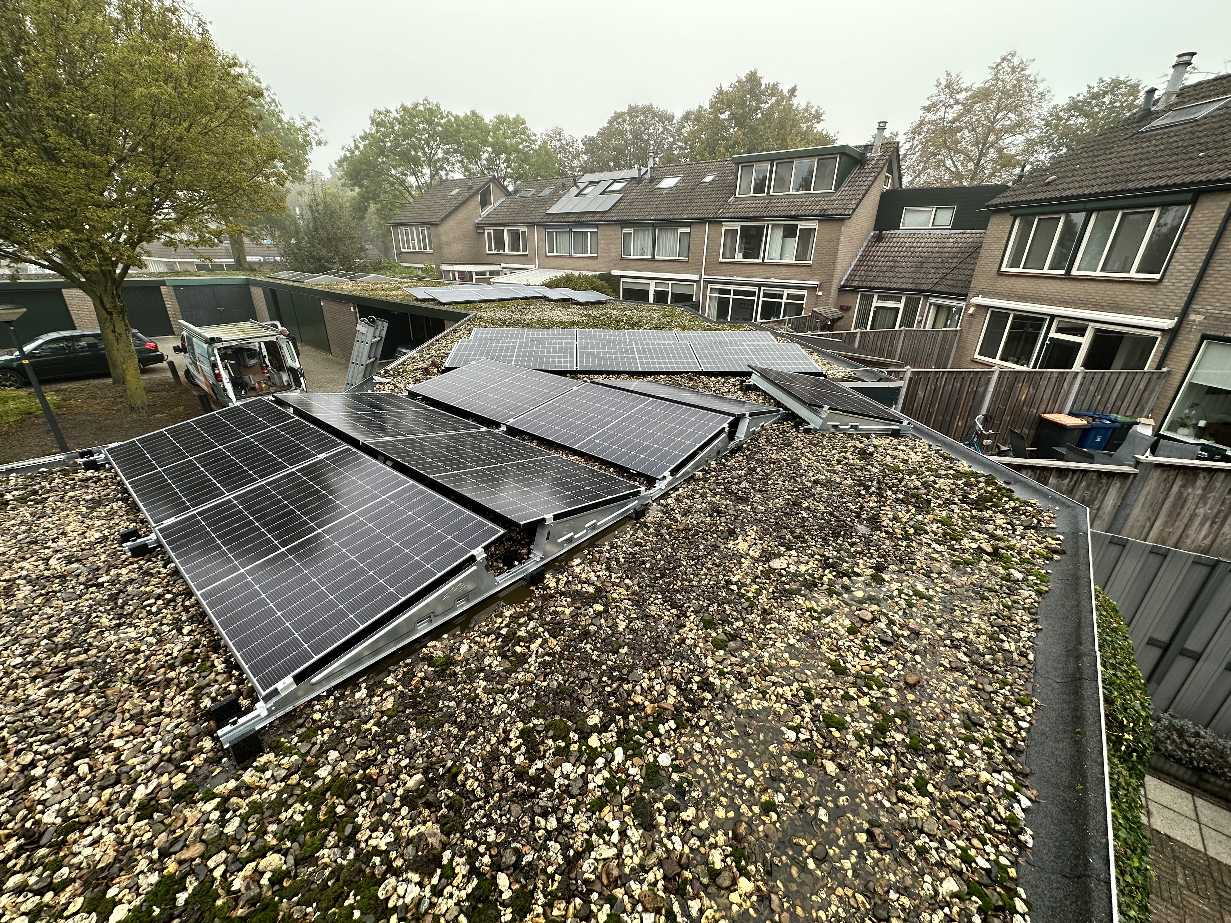De installatie toont zonnepanelen op een schuin dak, bevestigd met metalen steunen. De omgeving is slecht zichtbaar door mist, maar het installatieproces lijkt gaande.