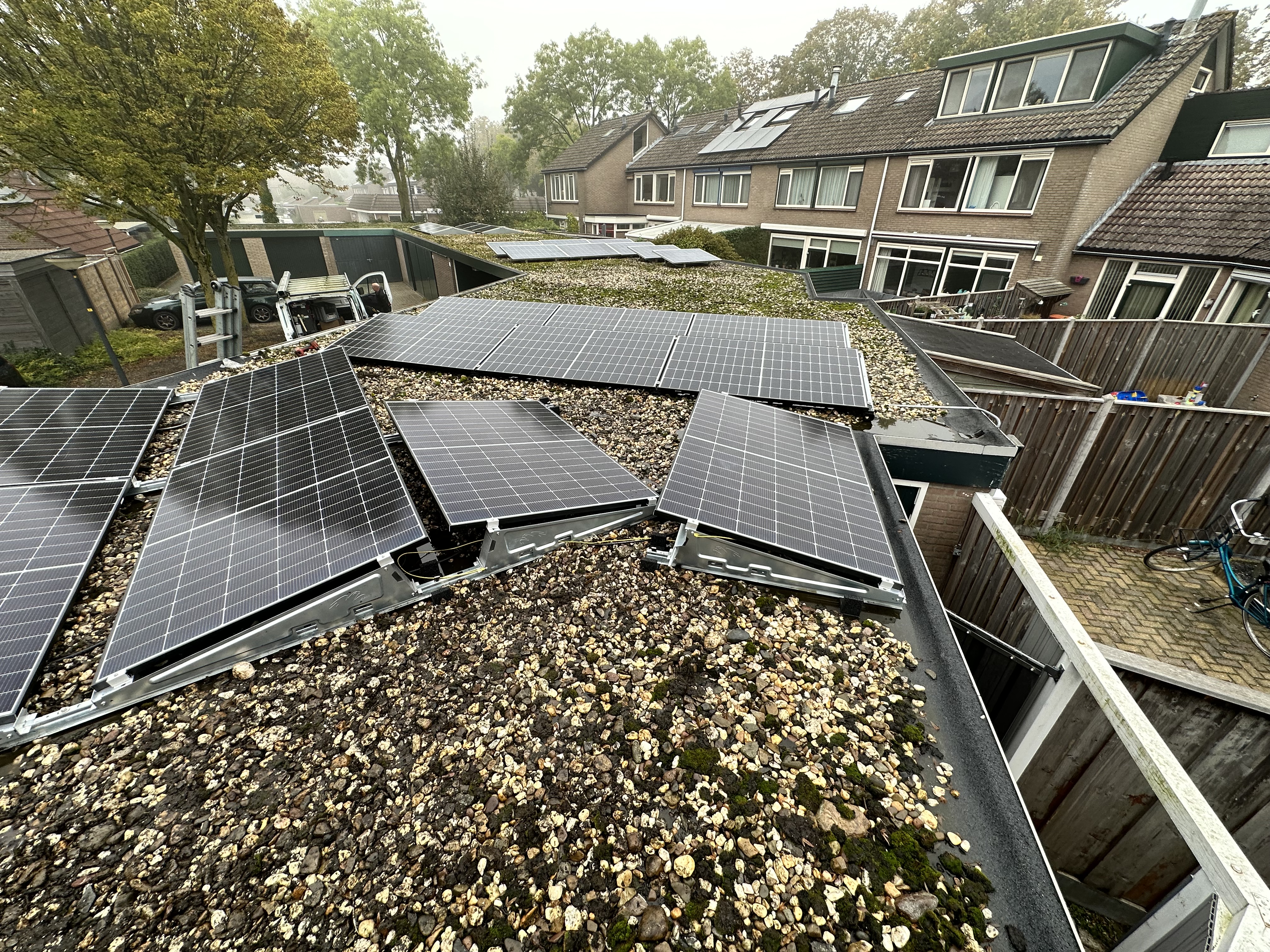 Deze installatie toont zonnepanelen bevestigd op een hellend dak, met een grindbedekking en diverse andere daken zichtbaar op de achtergrond.