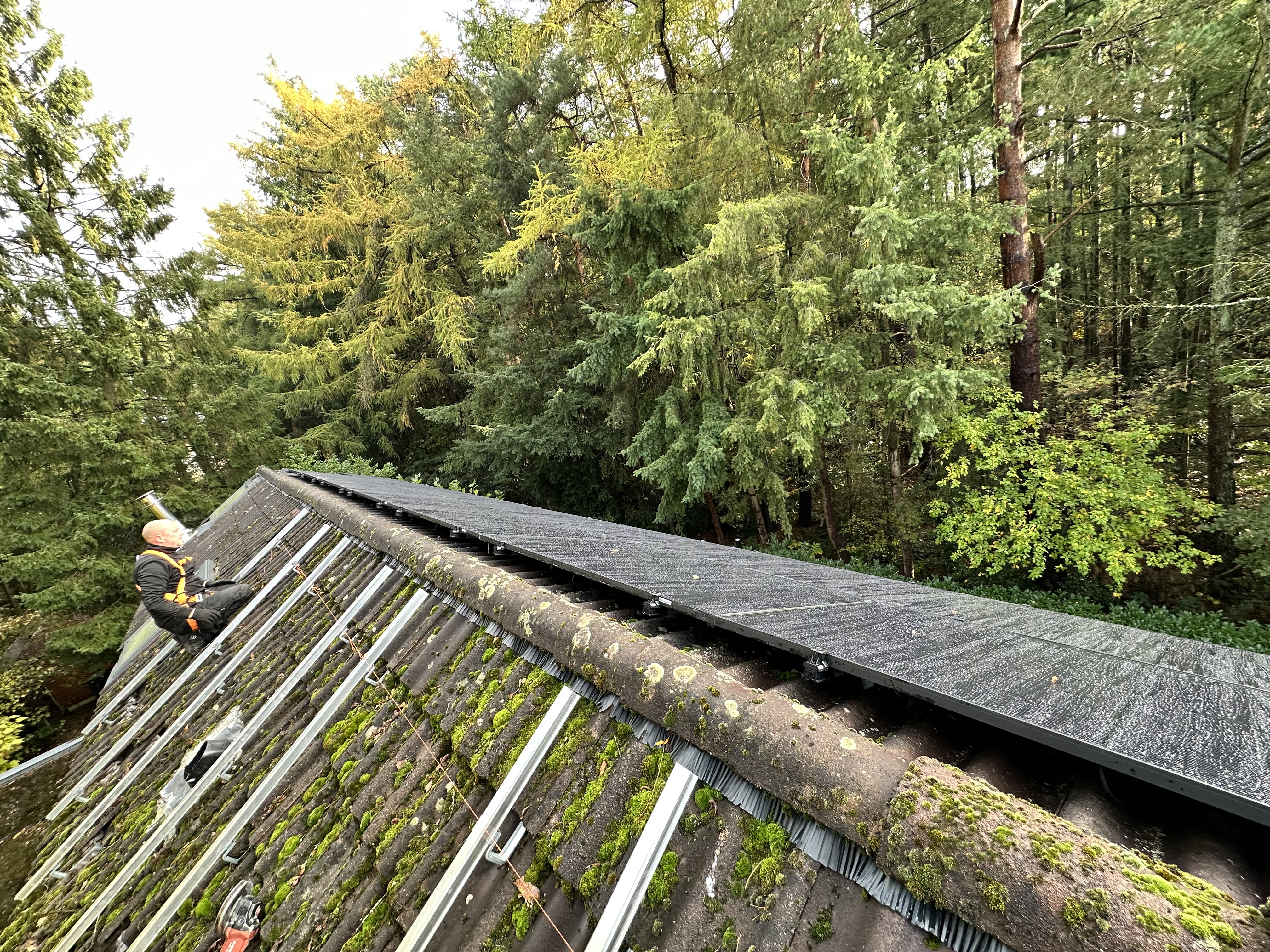 De foto toont een zonnepaneleninstallatie op een hellend dak, met een installateur die bezig is met de montage.