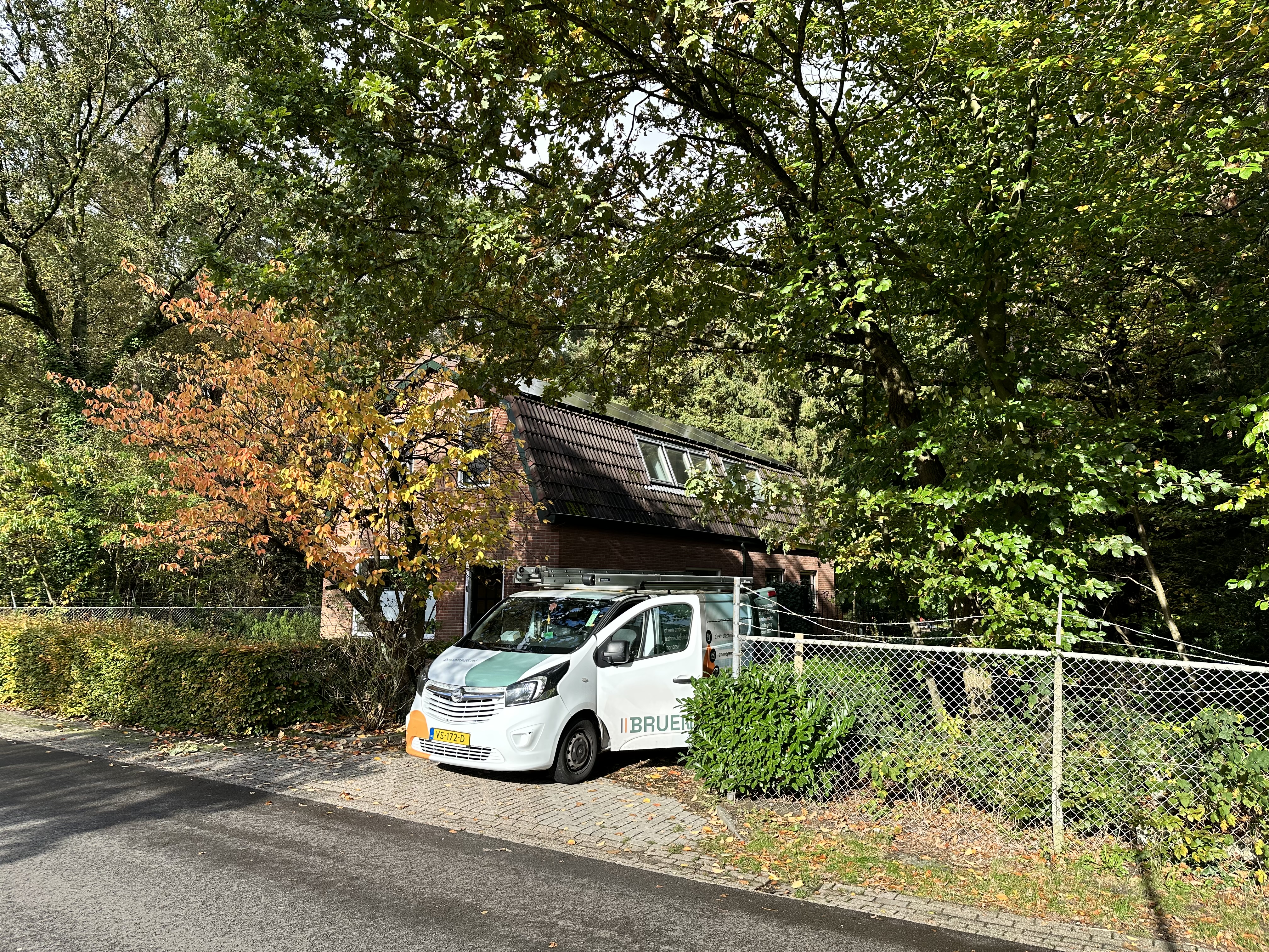 De afbeelding toont een huis met zonnepanelen op het dak en een installatievoertuig voor zonnepanelen in de nabijheid.