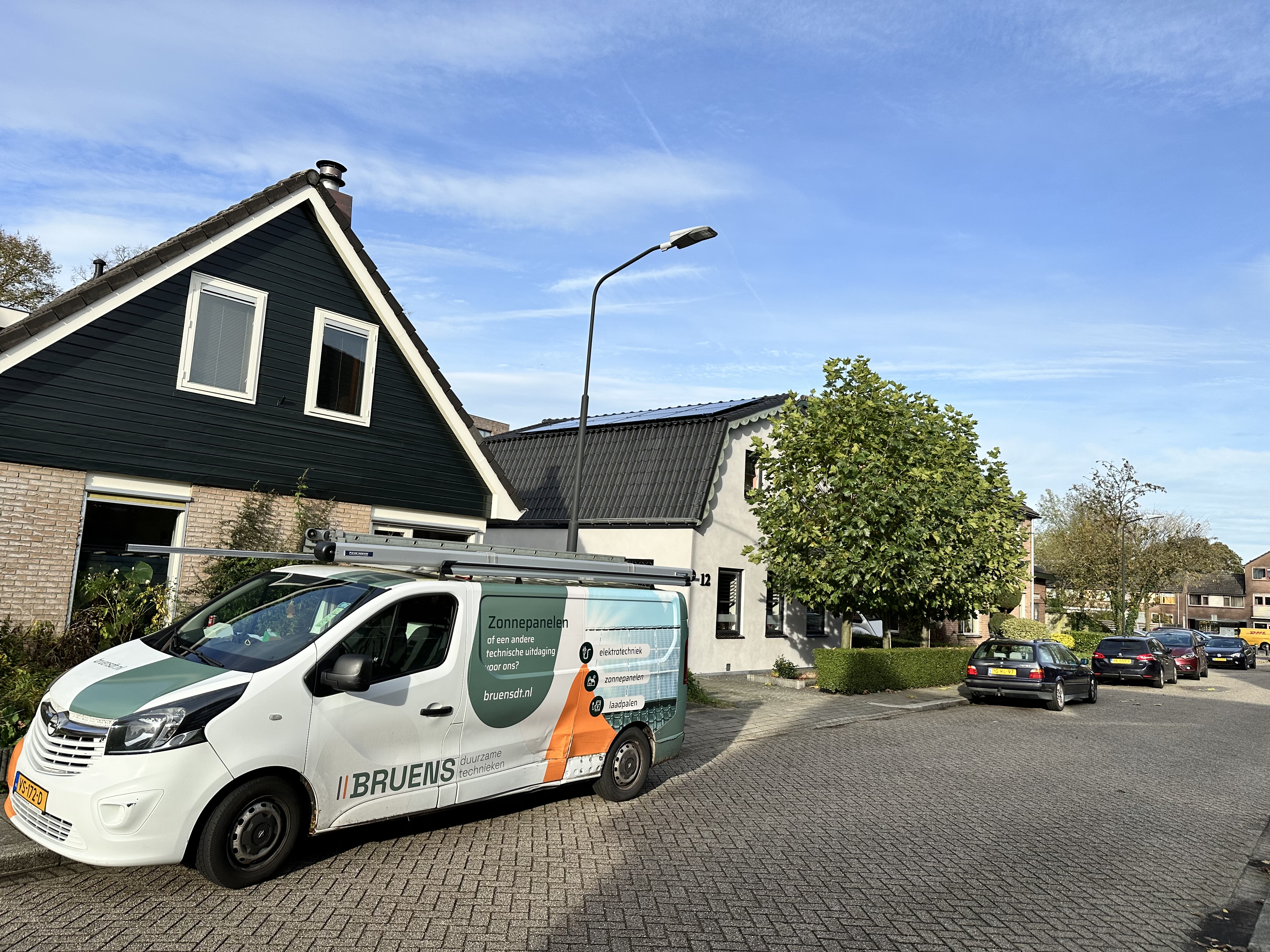 Een montagewagen staat geparkeerd voor een woning met zonnepanelen op het dak. De installatie is bezig of net afgerond.