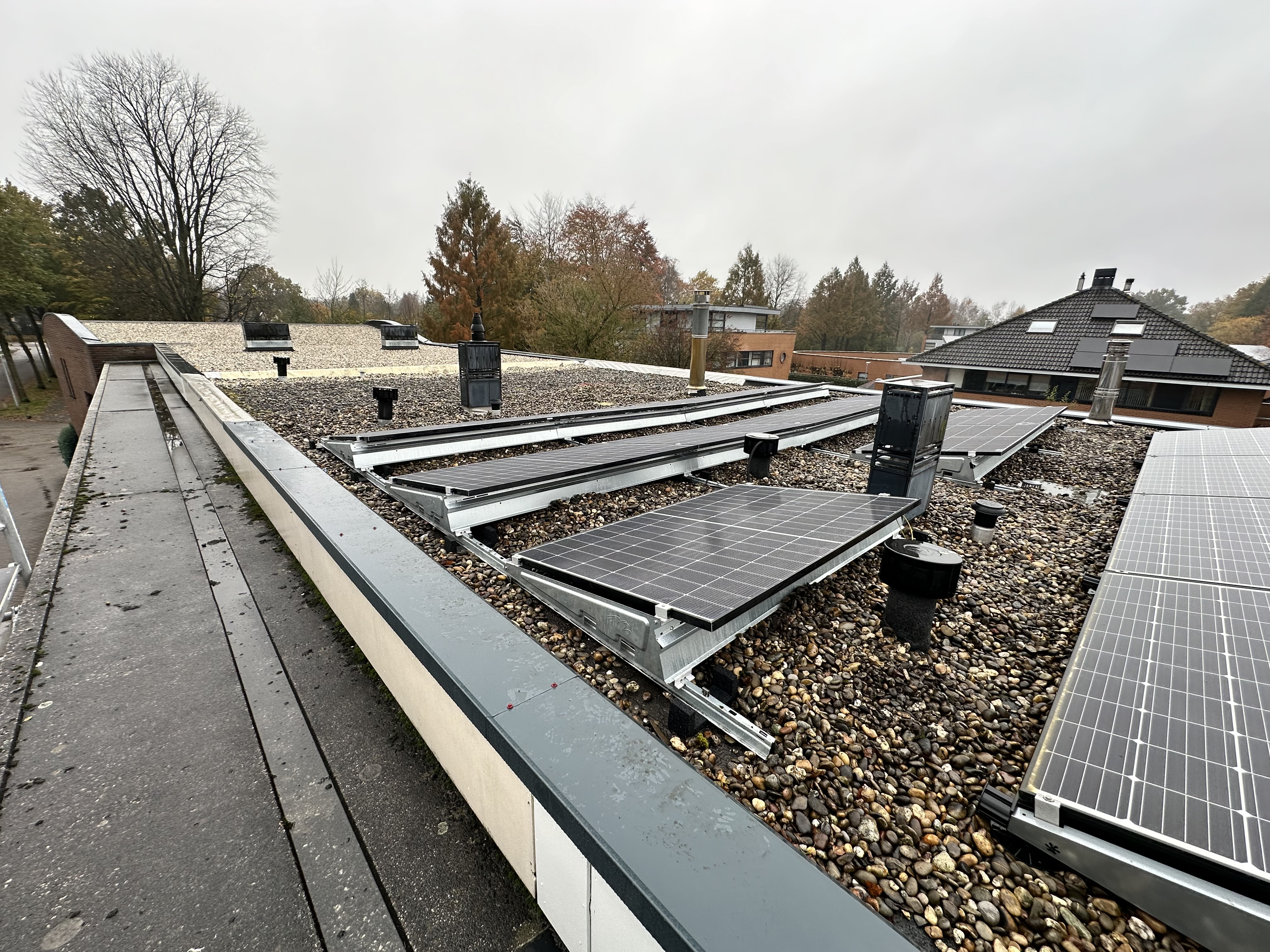 Deze installatie toont zonnepanelen die zijn bevestigd op een plat dak met grindbedekking.