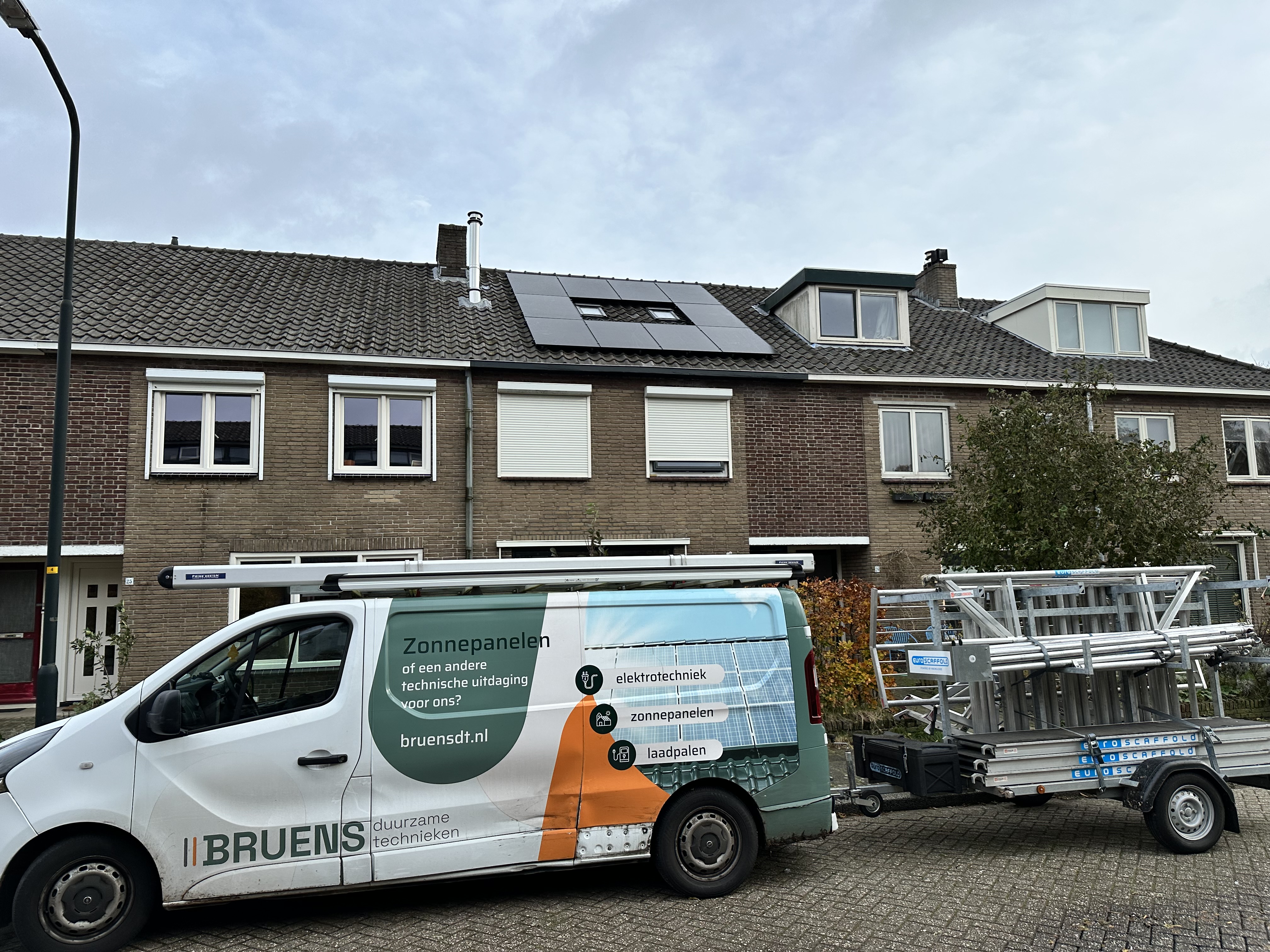 De foto toont een woning met zonnepanelen op het dak en een installatievoertuig van een zonnepaneelbedrijf ervoor.