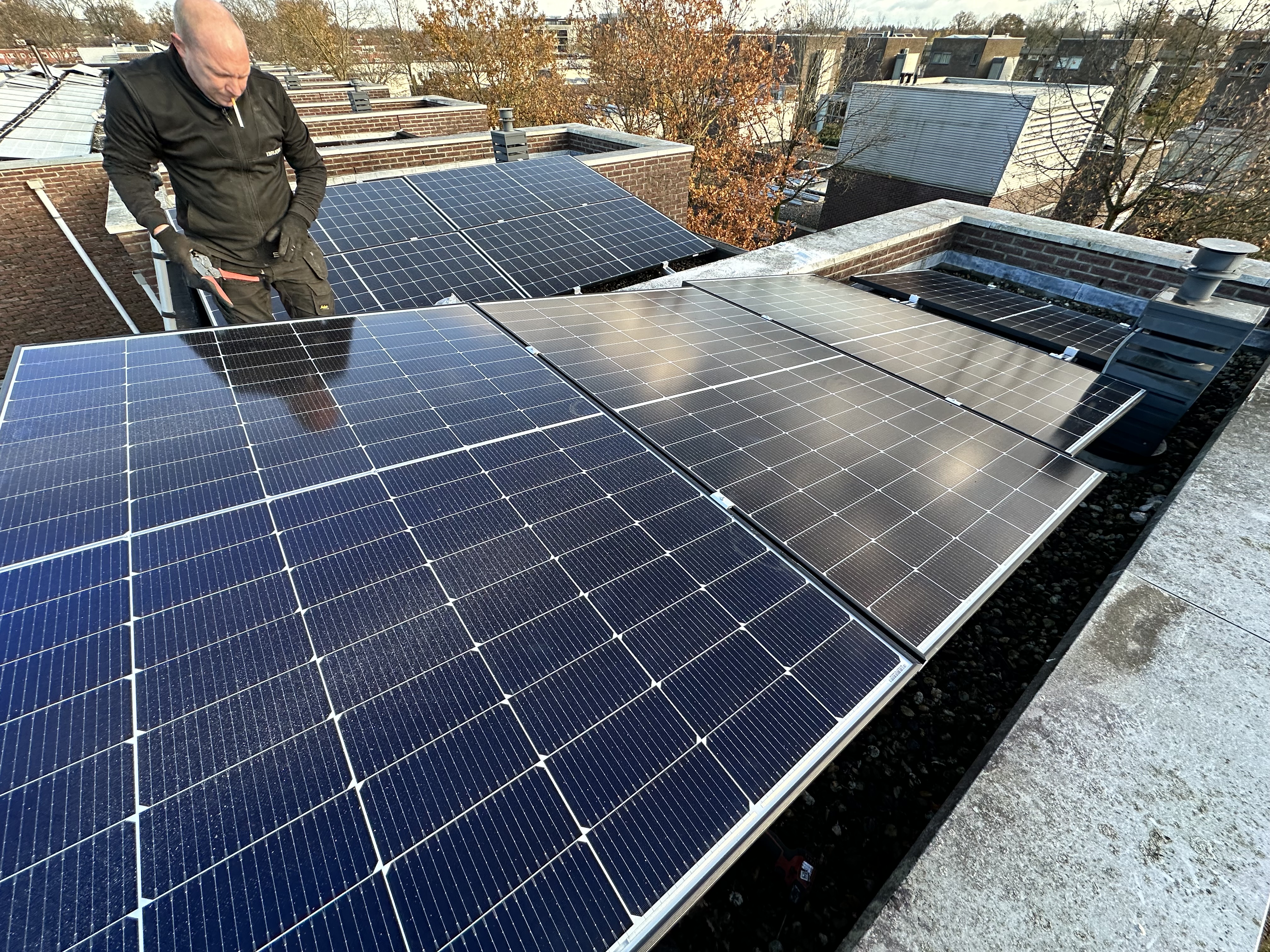 Een installatie van zonnepanelen op een plat dak, met een technicus die een van de panelen inspecteert.