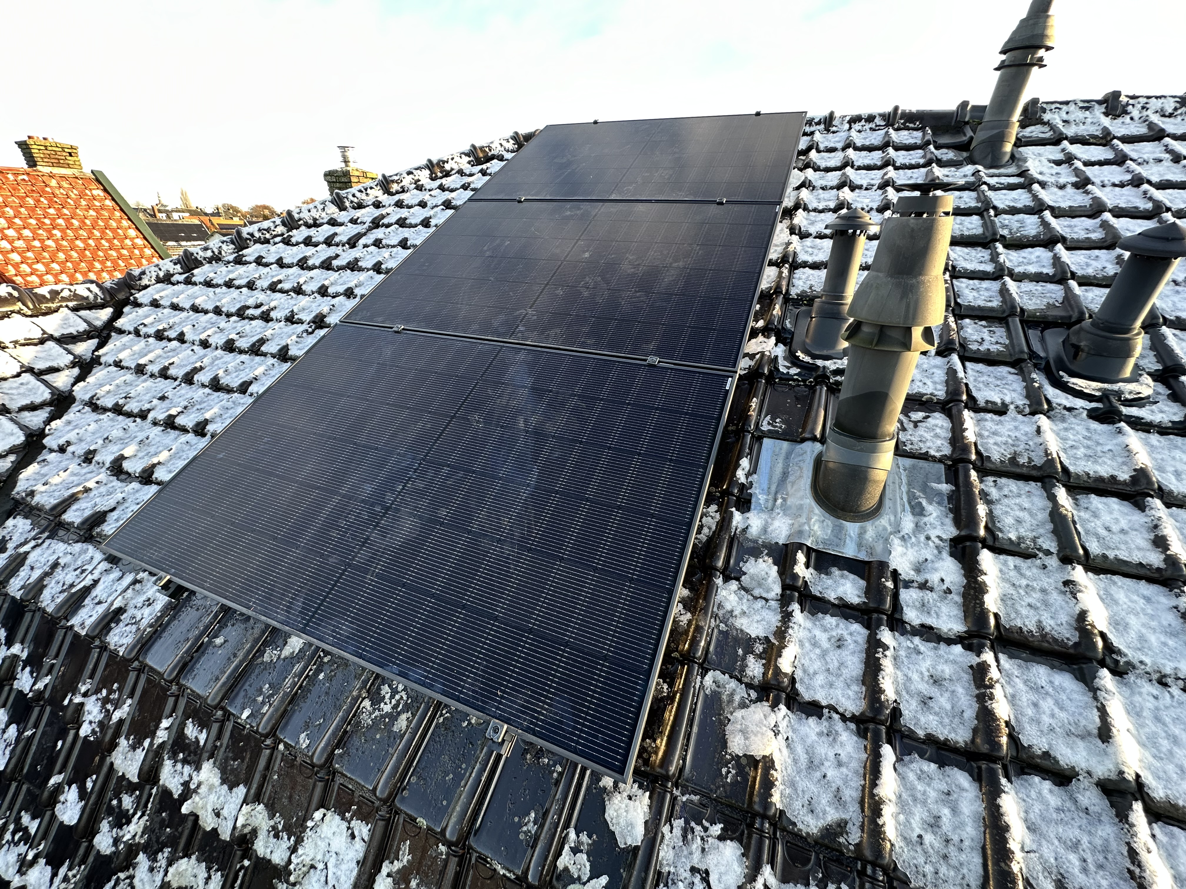 De foto toont een installatie van zonnepanelen op een schuin dak met sneeuwresten.