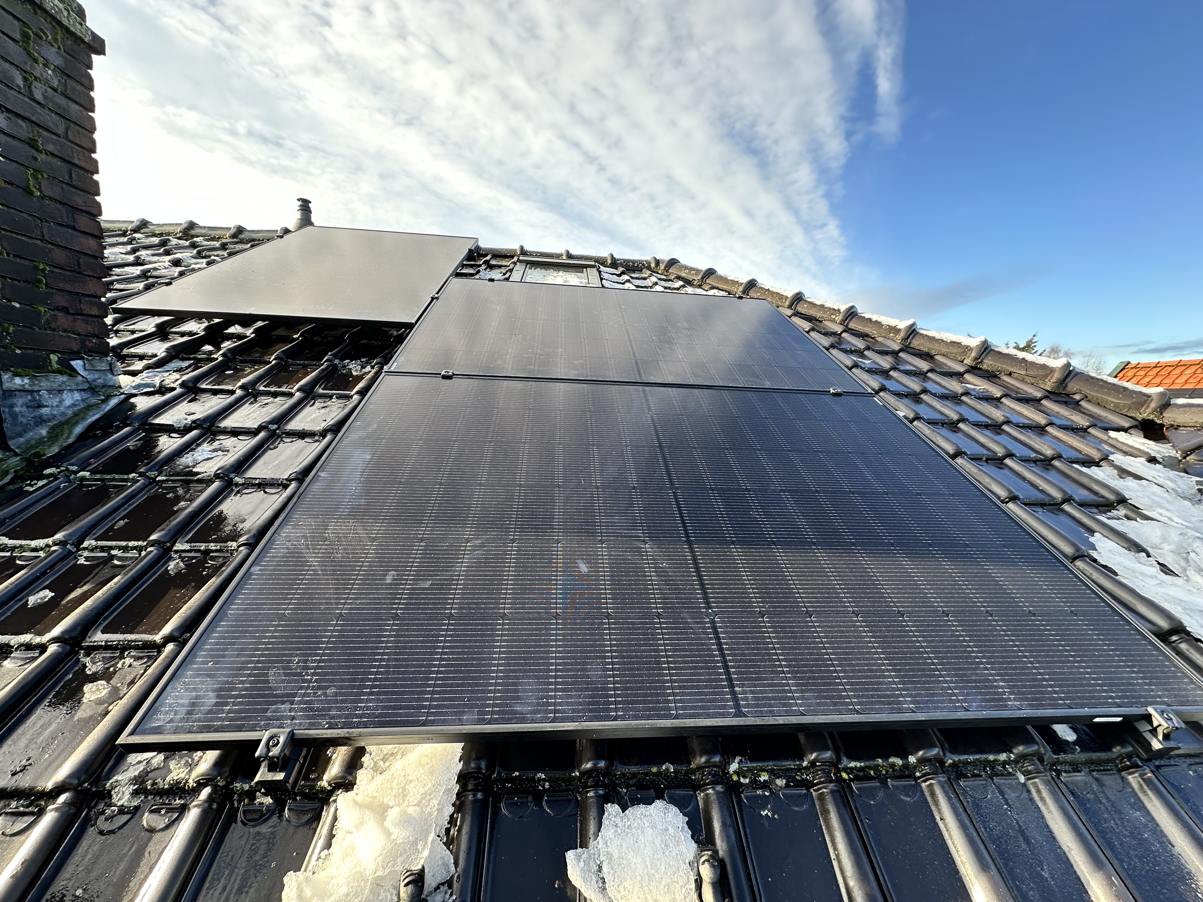 Een installatie van zonnepanelen op een hellend dak, zichtbaar zijn enkele panelen met een blauwe lucht op de achtergrond.