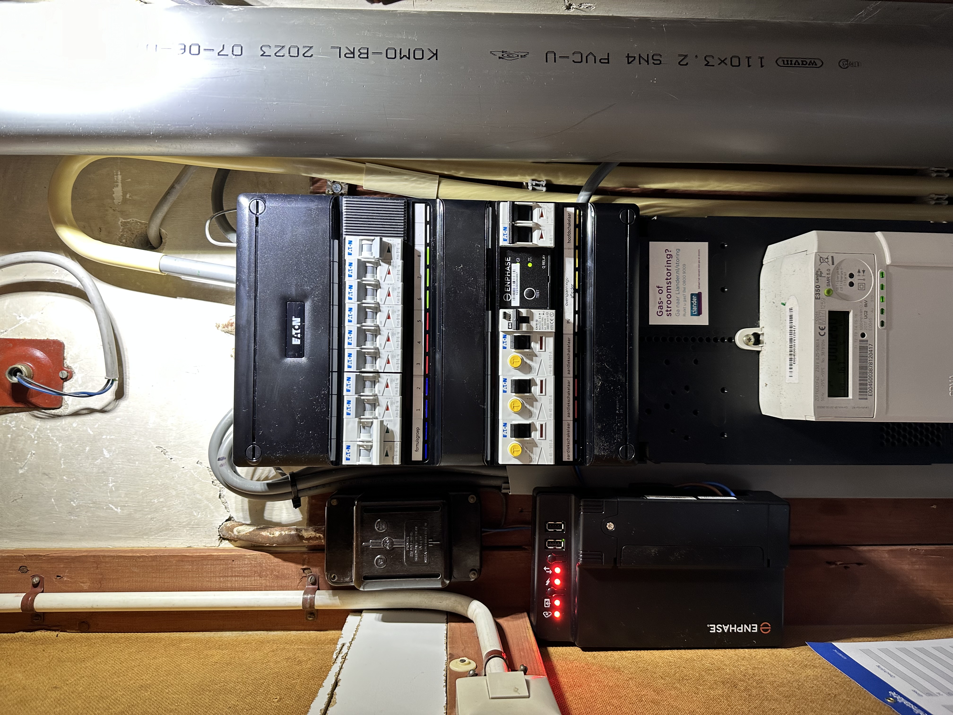 De afbeelding toont een meterkast met diverse elektrische componenten, inclusief een Enphase-apparaat, dat mogelijk gerelateerd is aan een zonnepaneleninstallatie.