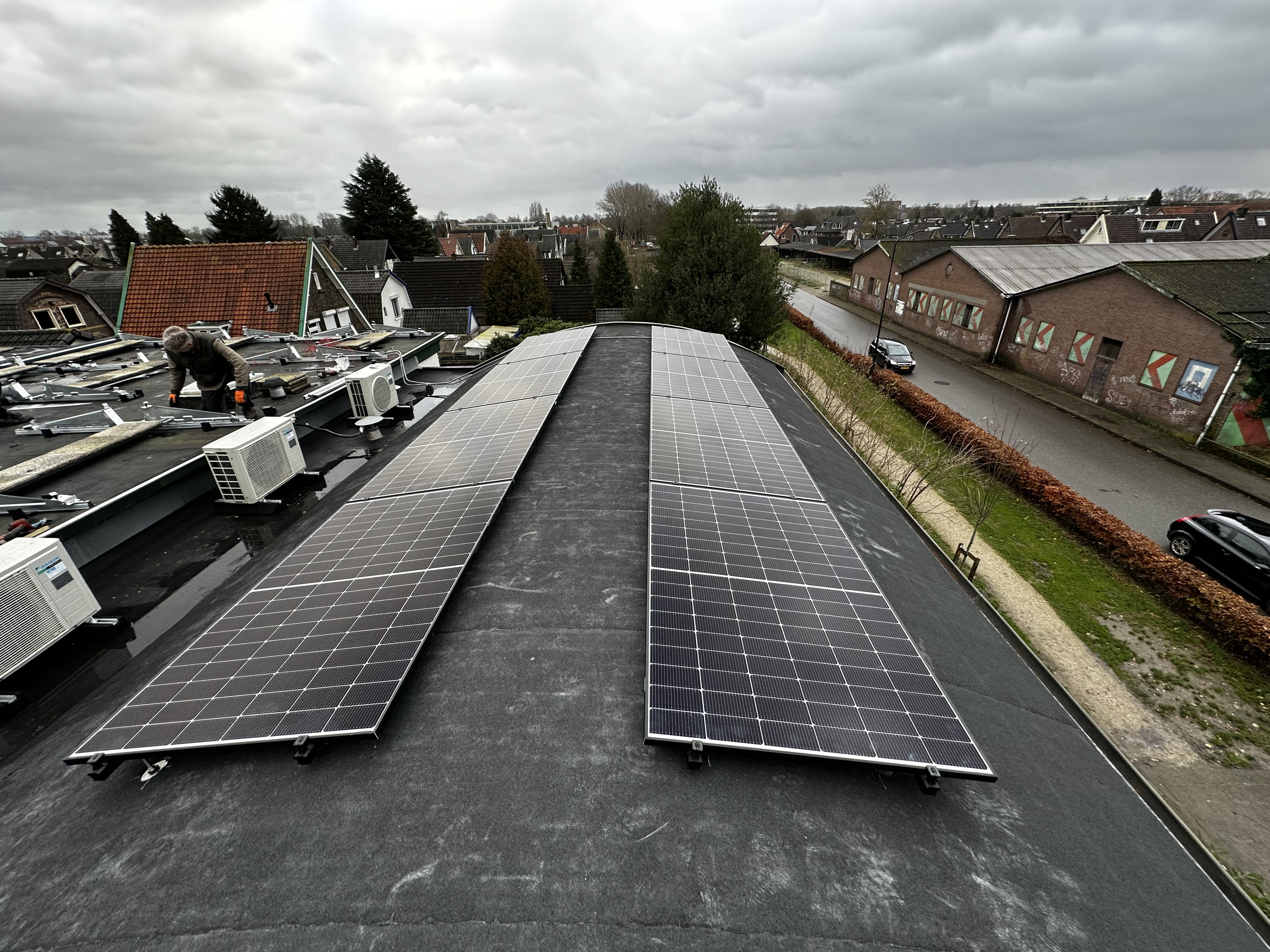 Installatie van zonnepanelen op een plat dak, met een technicus die werkt aan de montage.