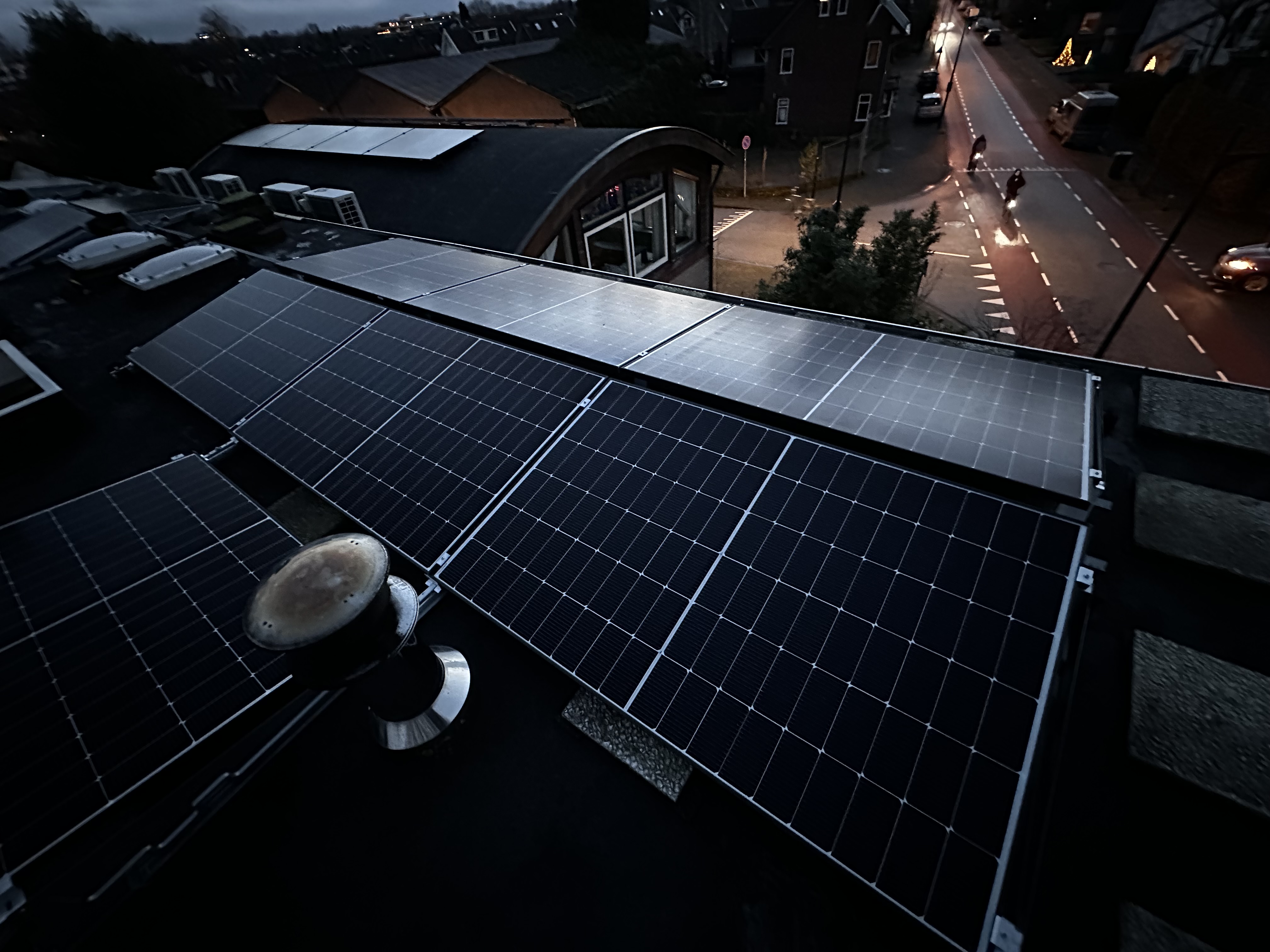 De afbeelding toont zonnepanelen op een dak, mooi gepositioneerd om zonlicht te vangen, met een stadsomgeving op de achtergrond.