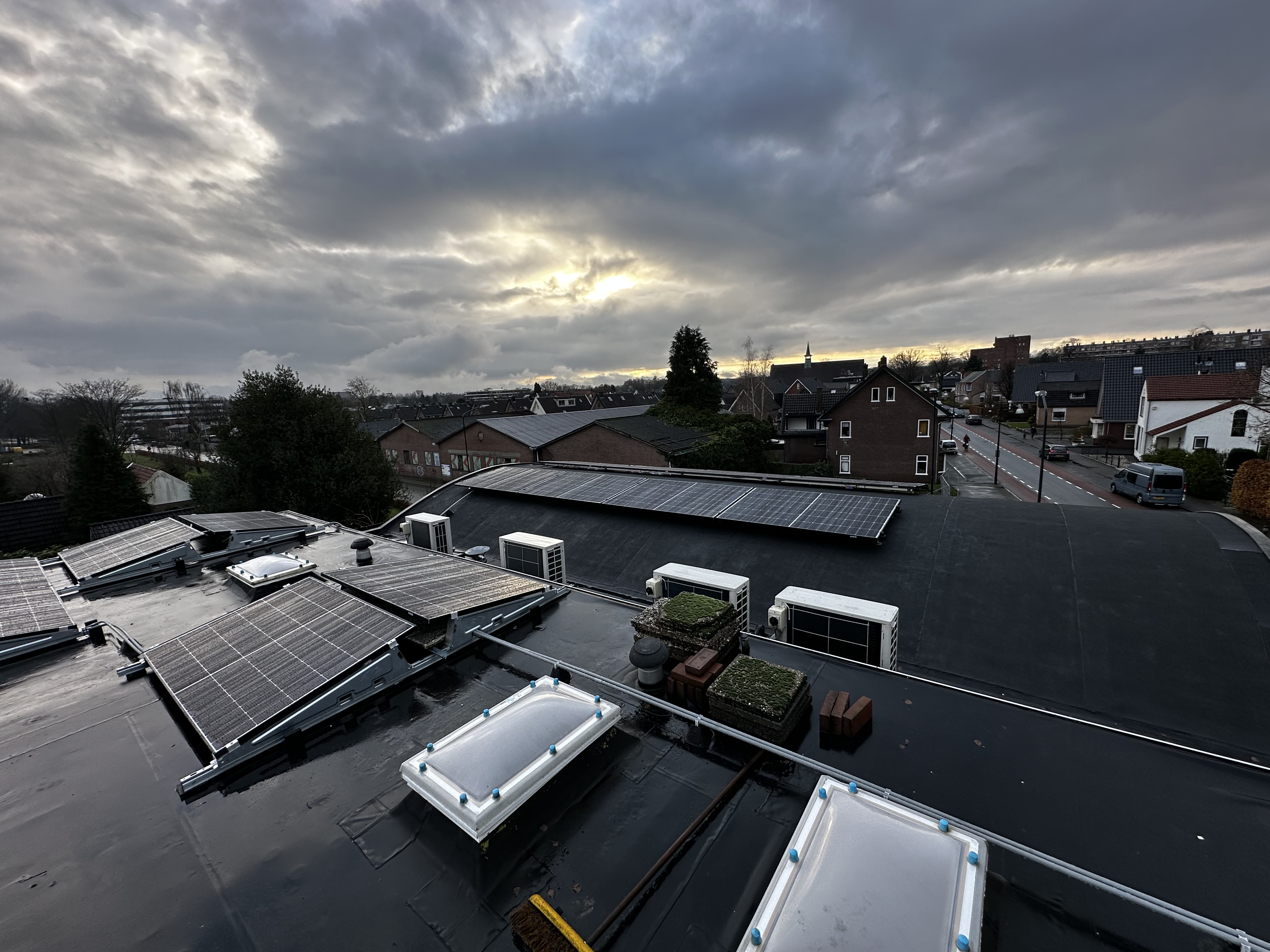 Deze installatie toont zonnepanelen op een plat dak, met uitzicht op een buurt. De panelen zijn strategisch geplaatst voor optimale blootstelling aan zonlicht.