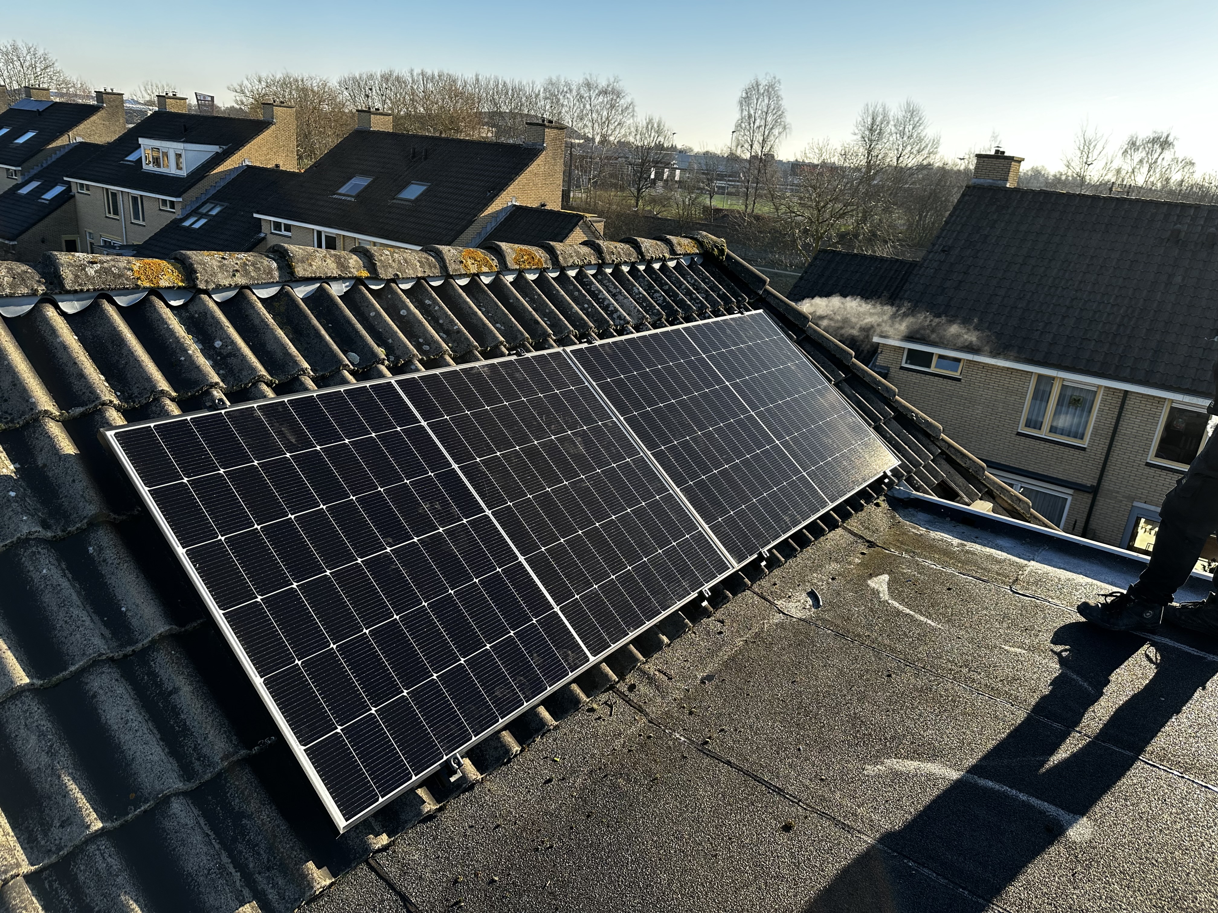 De afbeelding toont een installatie van zonnepanelen op het dak van een woning, gericht op maximale blootstelling aan zonlicht.