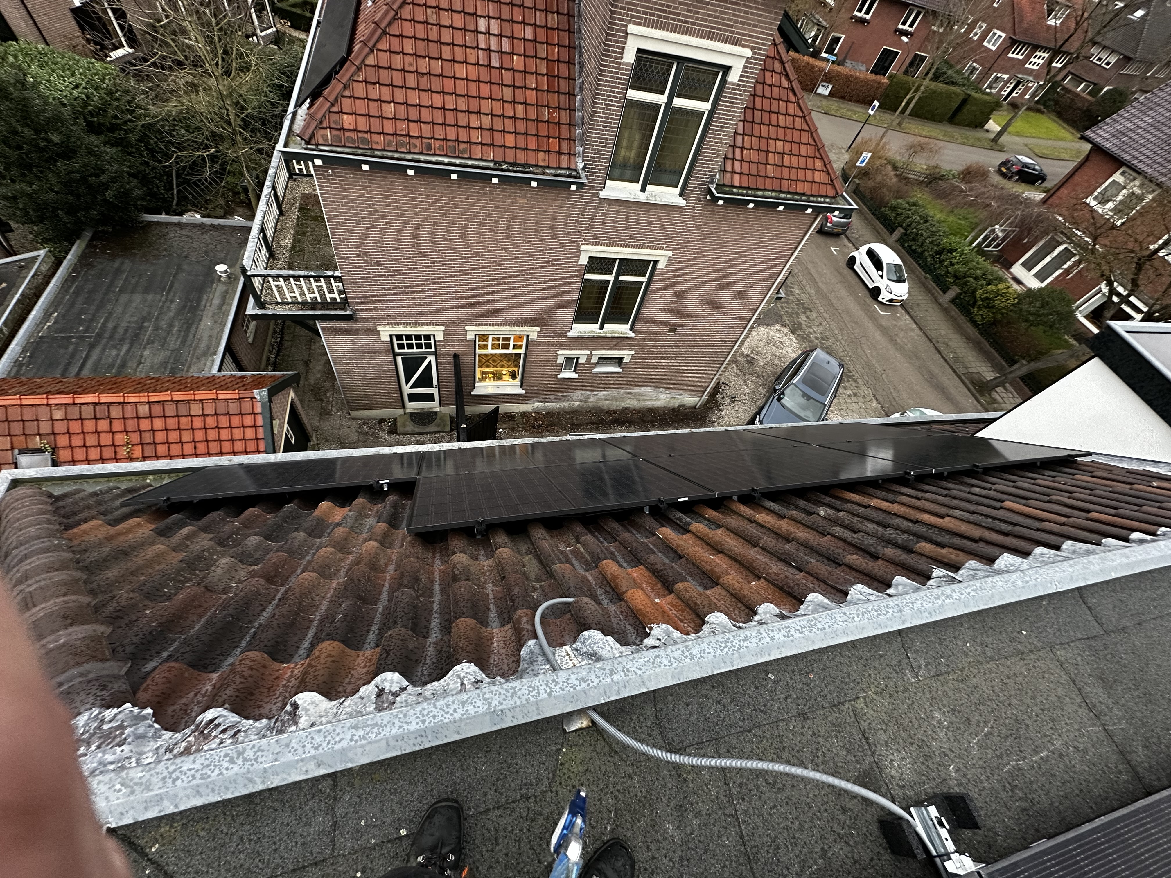 De foto toont zonnepanelen die zijn geïnstalleerd op een hellend dak, met een overzicht van de omliggende gebouwen.