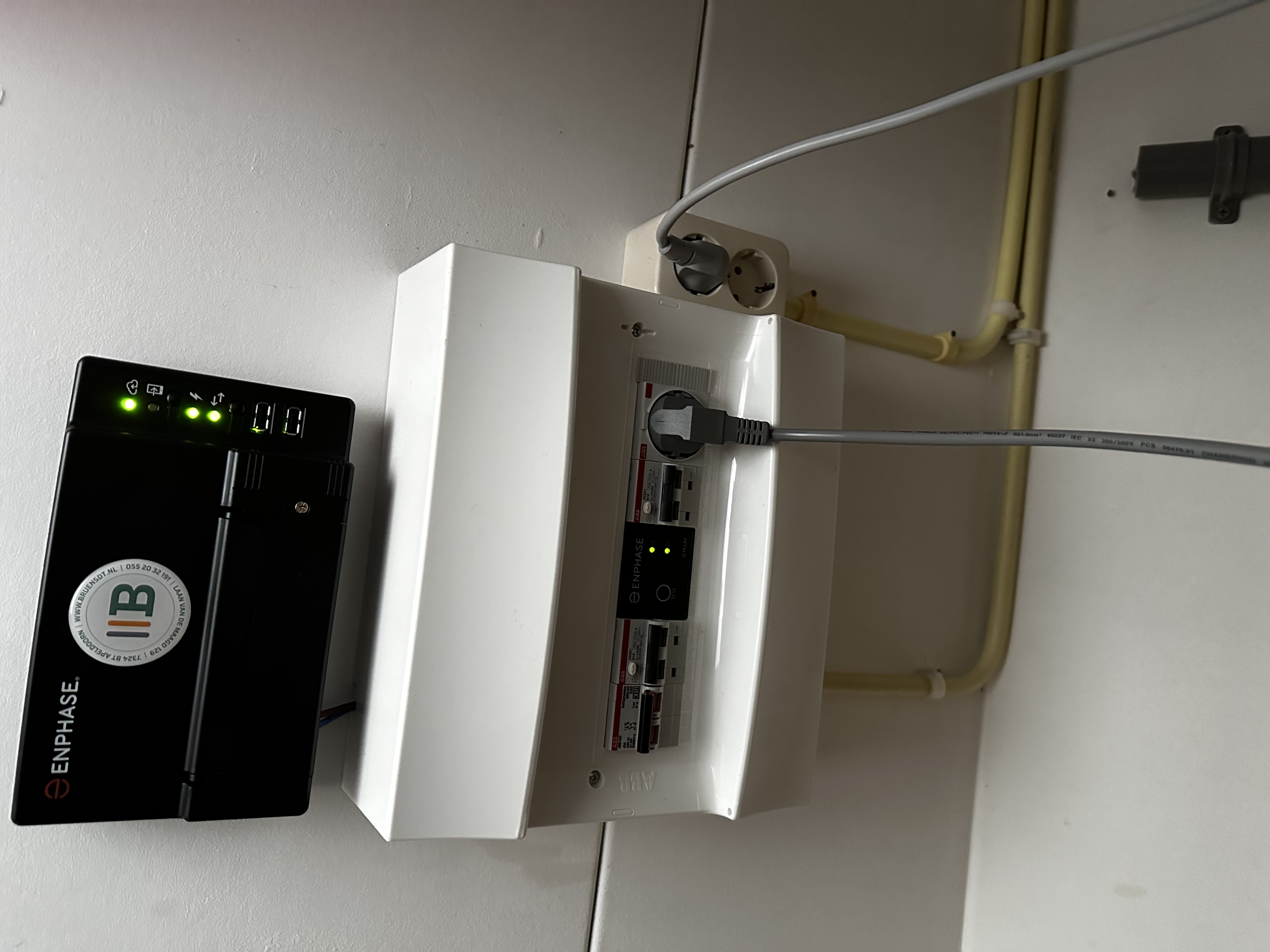 De afbeelding toont een deel van een meterkast met een Enphase apparaat en bekabeling, wat wijst op een installatie gerelateerd aan zonnepanelen.