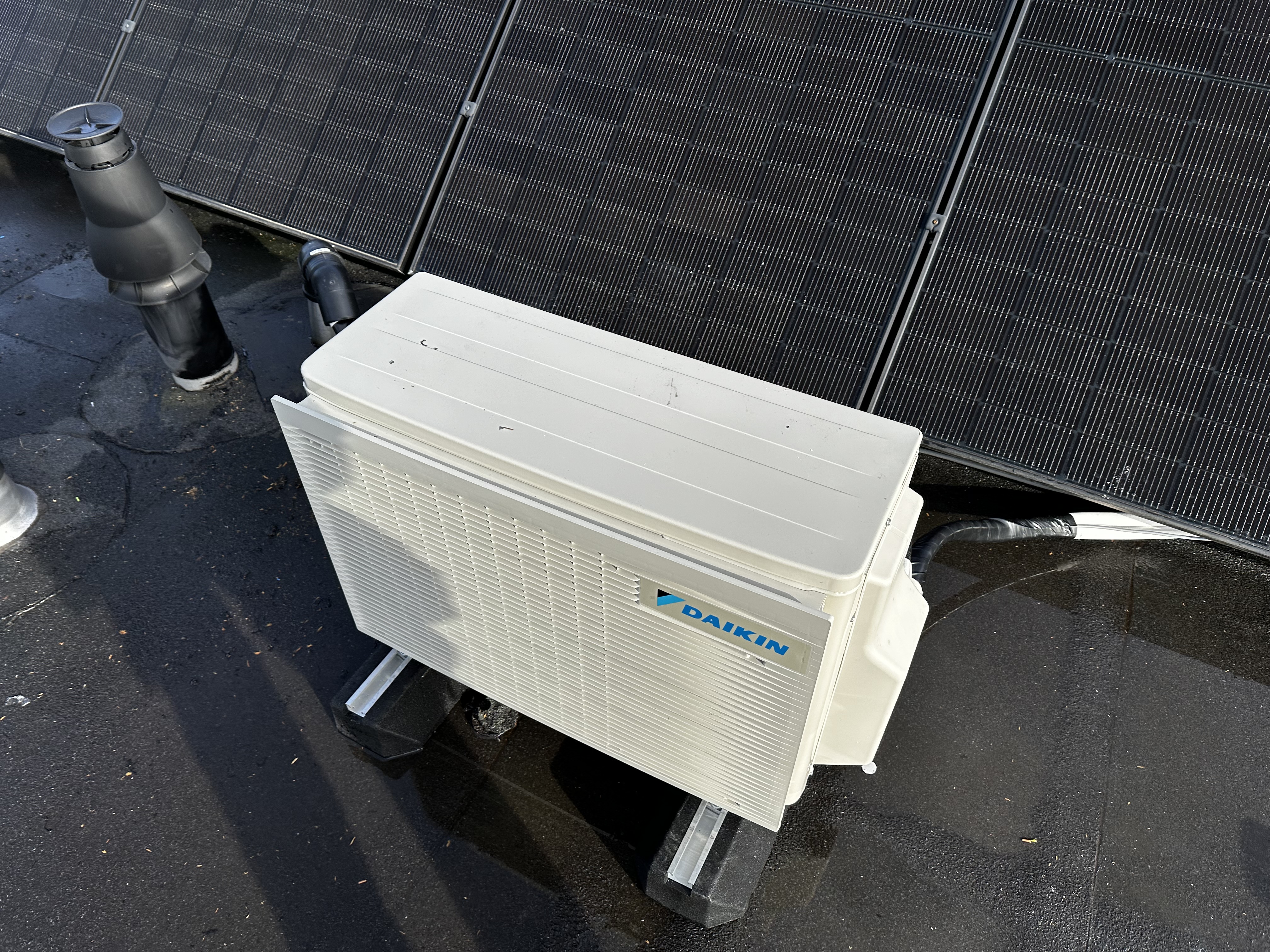 Een buitenunit van een Daikin airconditioningsysteem, geplaatst op een dak met zonnepanelen.