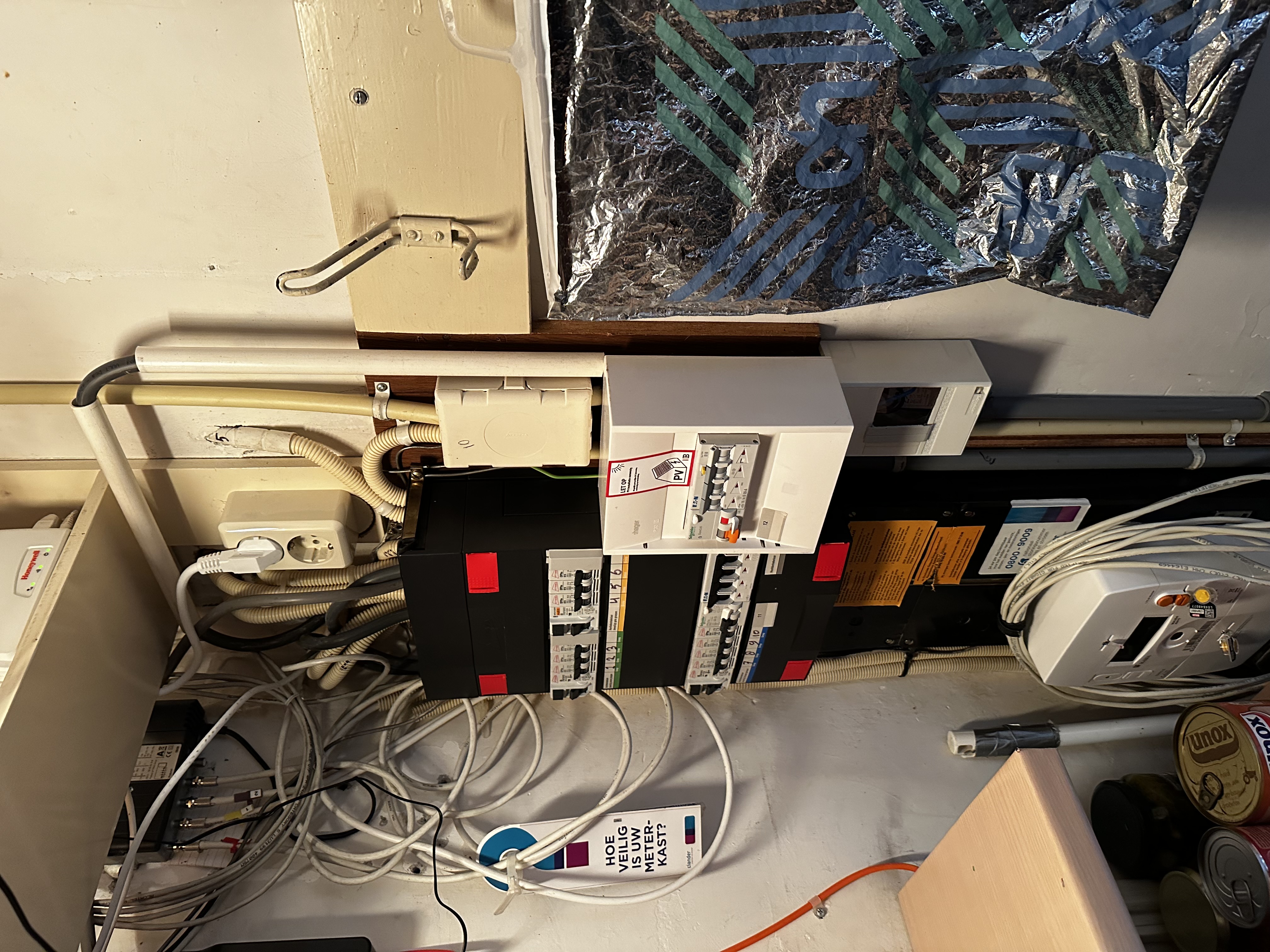 De afbeelding toont een meterkast met diverse schakelaars en bedrading, typisch voor een installatie van zonnepanelen, waaronder de omvormer.