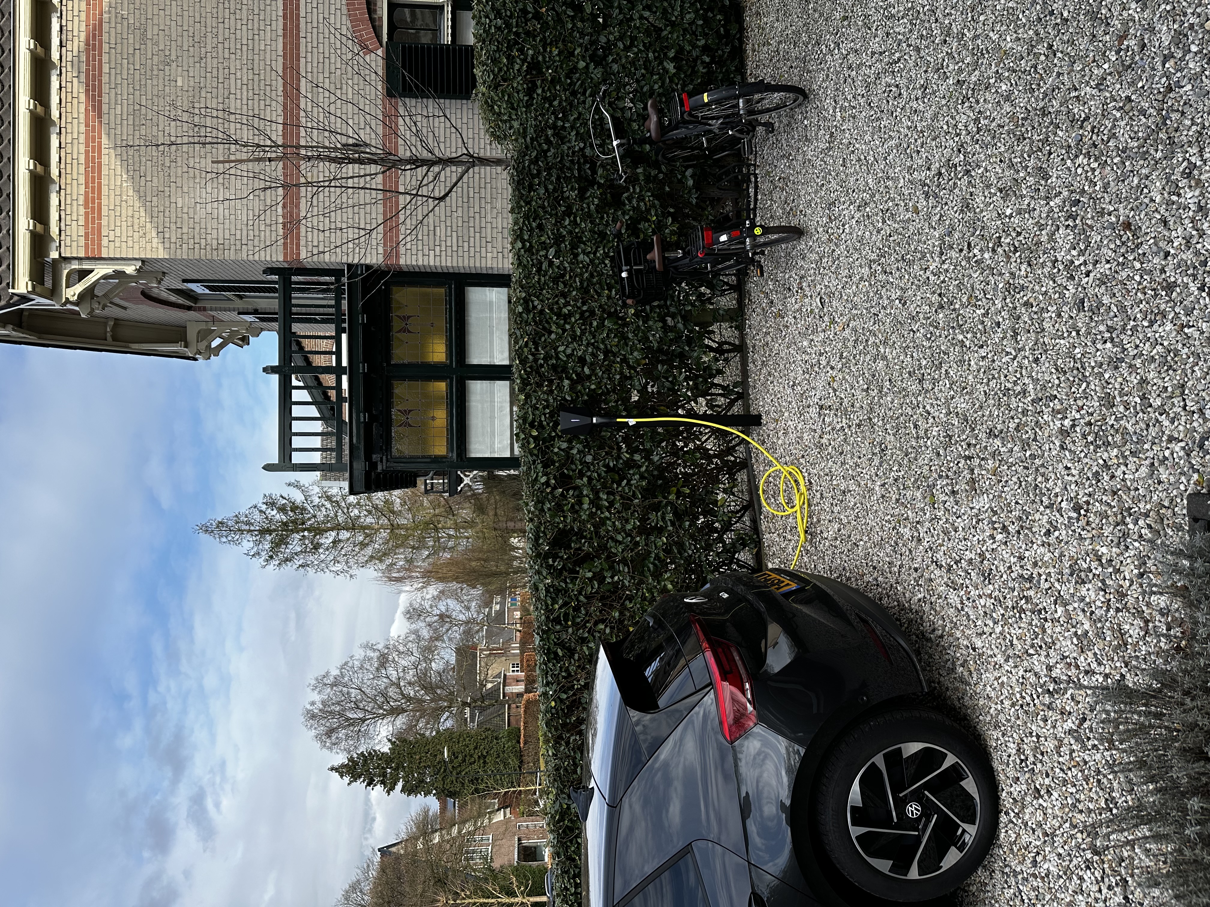 Een laadpaal voor elektrische voertuigen is in gebruik, met een auto ernaast en fietsen in de buurt.