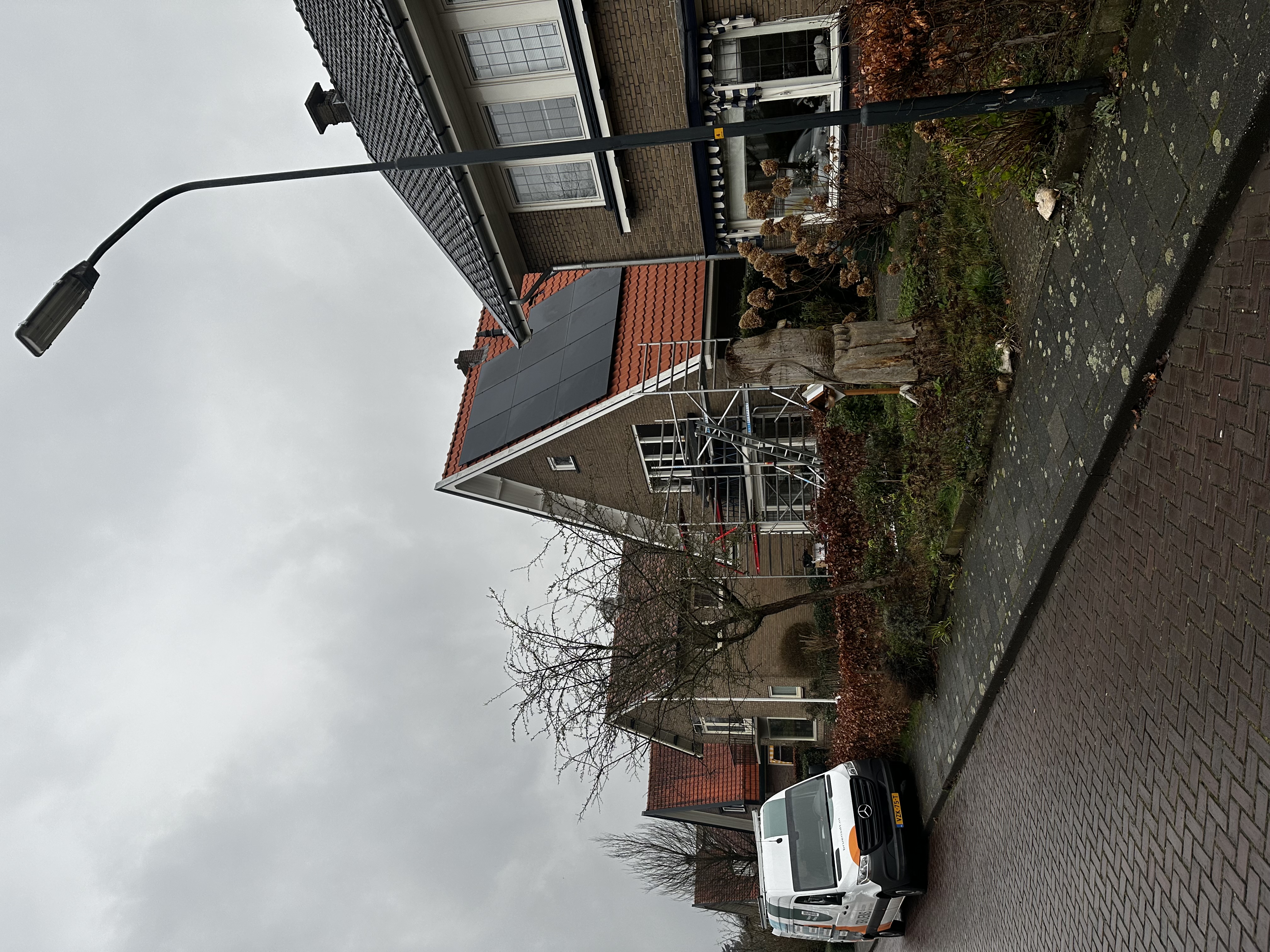 De foto toont een woning met zonnepanelen op het dak, tijdens een installatieproces met steigers zichtbaar.