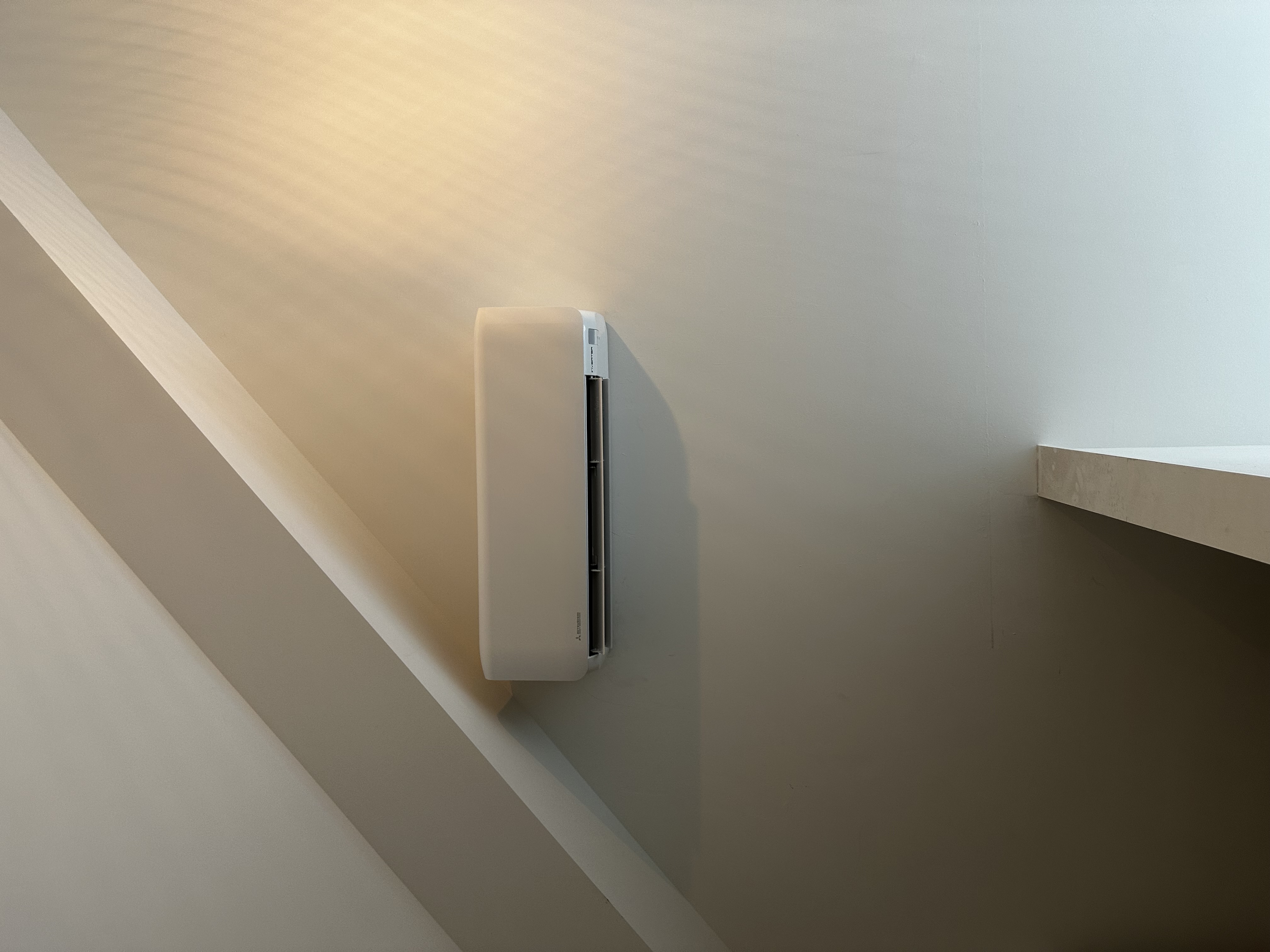 Een wandgemonteerde airconditioner geplaatst in een hoek met een schuin plafond.