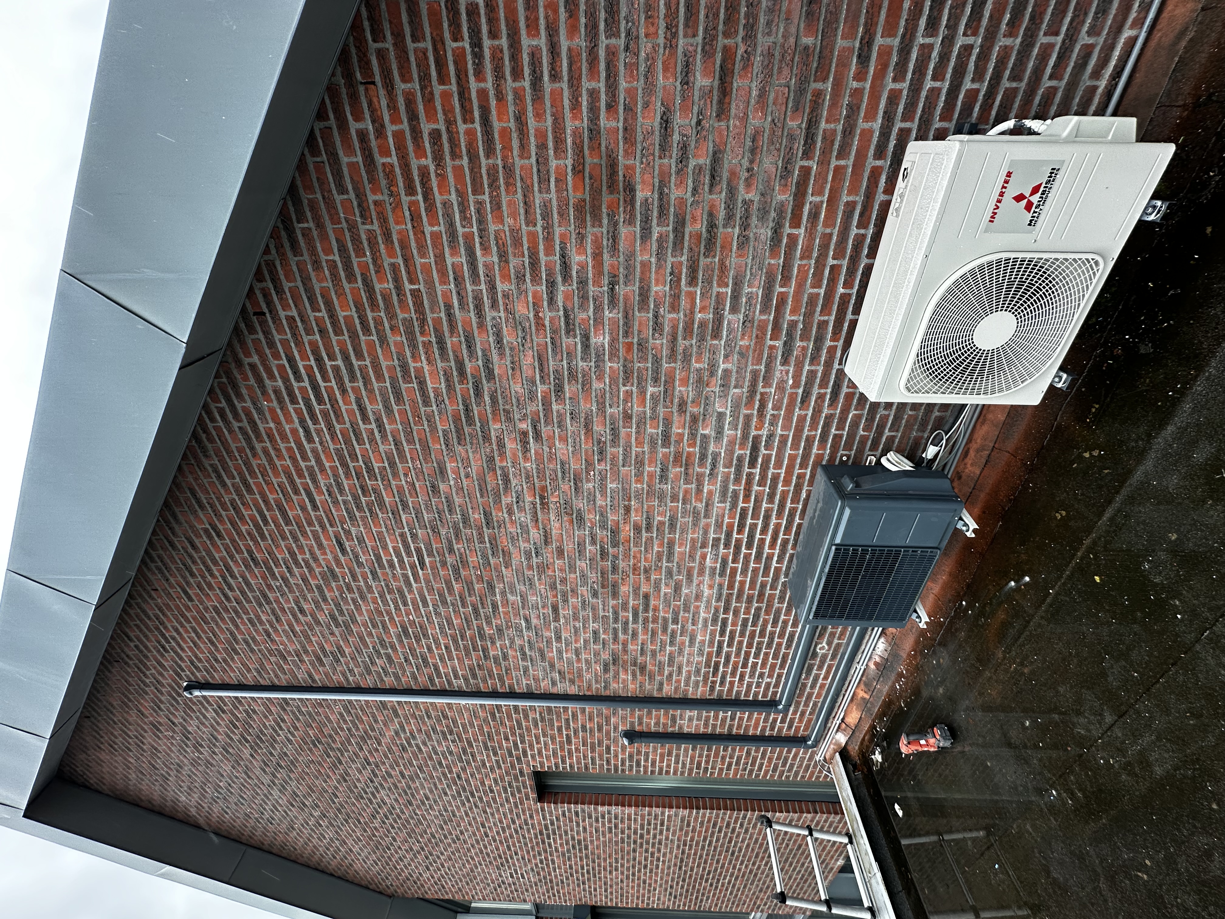 De afbeelding toont een installatie van een airconditioning, met binnen- en buitenunits bevestigd aan de muur.