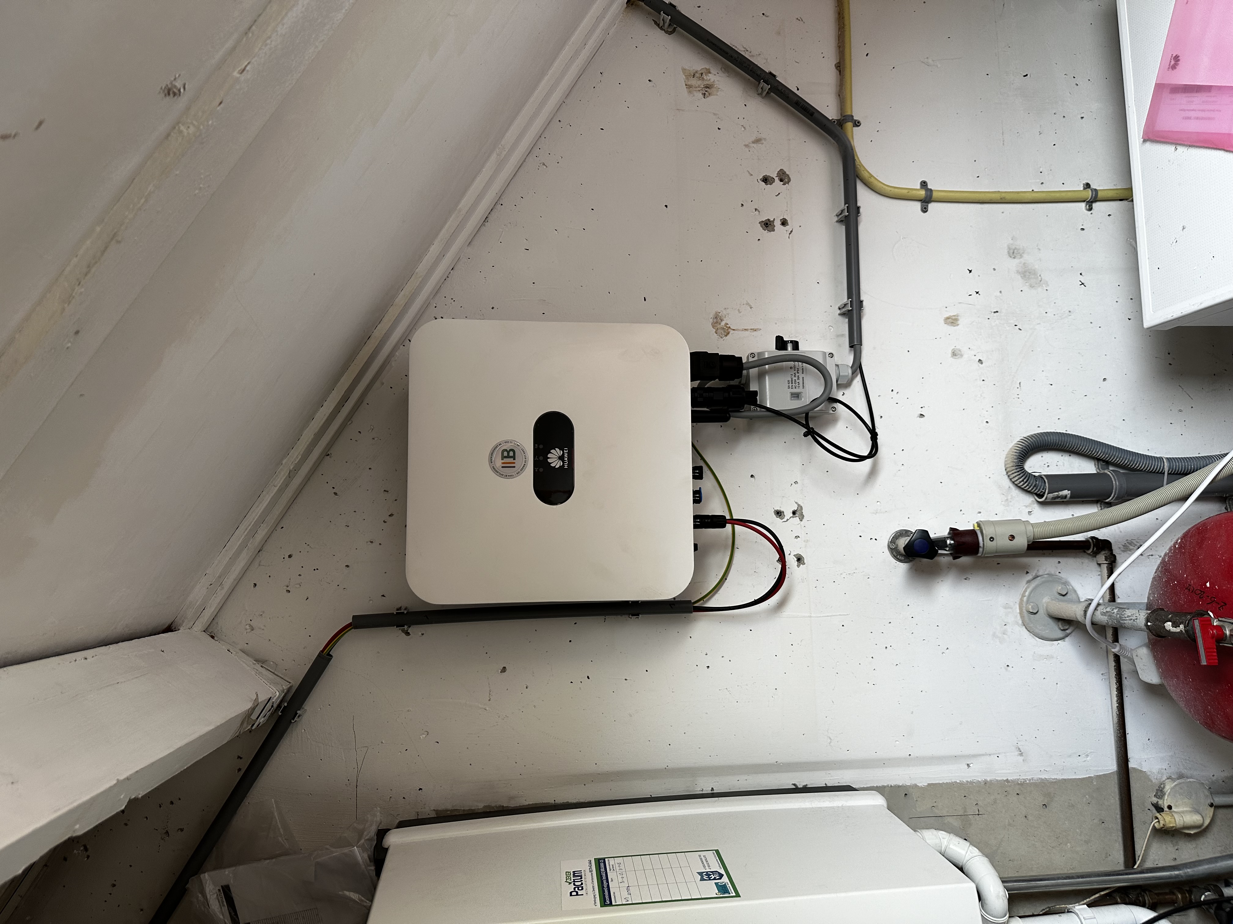 De installatie toont een omvormer voor zonnepanelen, welke de gelijkstroom van de panelen omzet in wisselstroom voor huishoudelijk gebruik.
