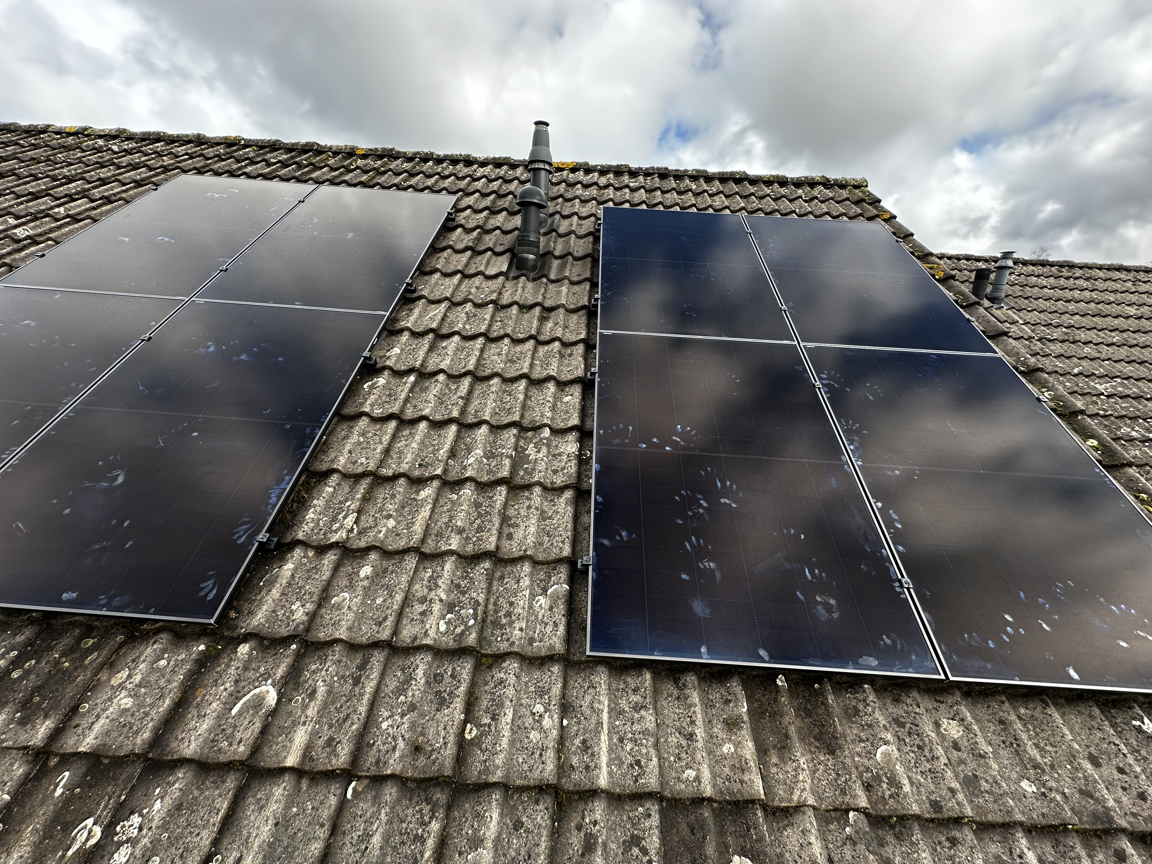 De installatie toont zonnepanelen op een schuin dak, met een duidelijke reflectie van de lucht op de panelen. Handafdrukken zijn zichtbaar op de panelen.