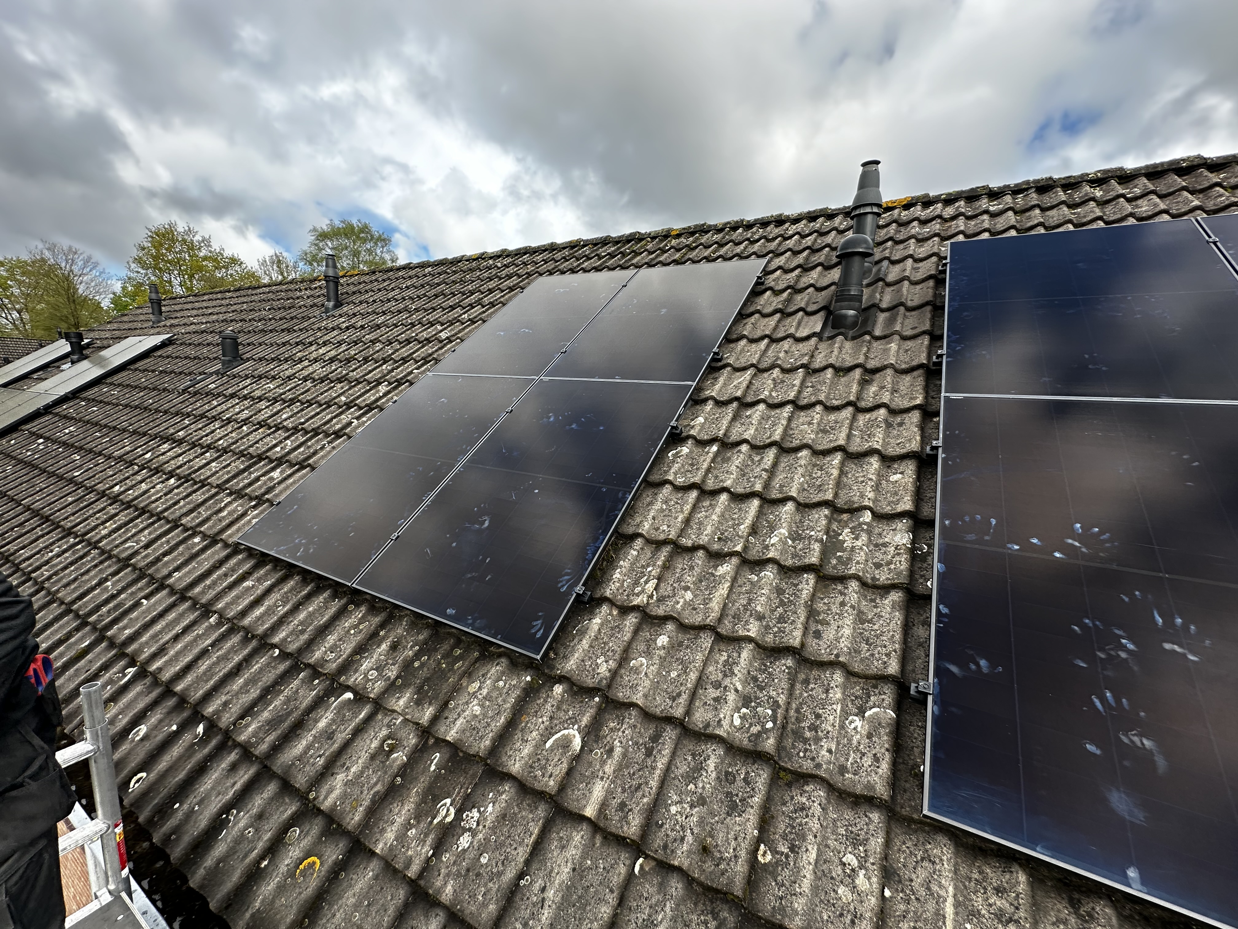 De foto toont een installatie van zonnepanelen op een hellend dak, met een duidelijk zicht op de panelen en de dakbedekking.