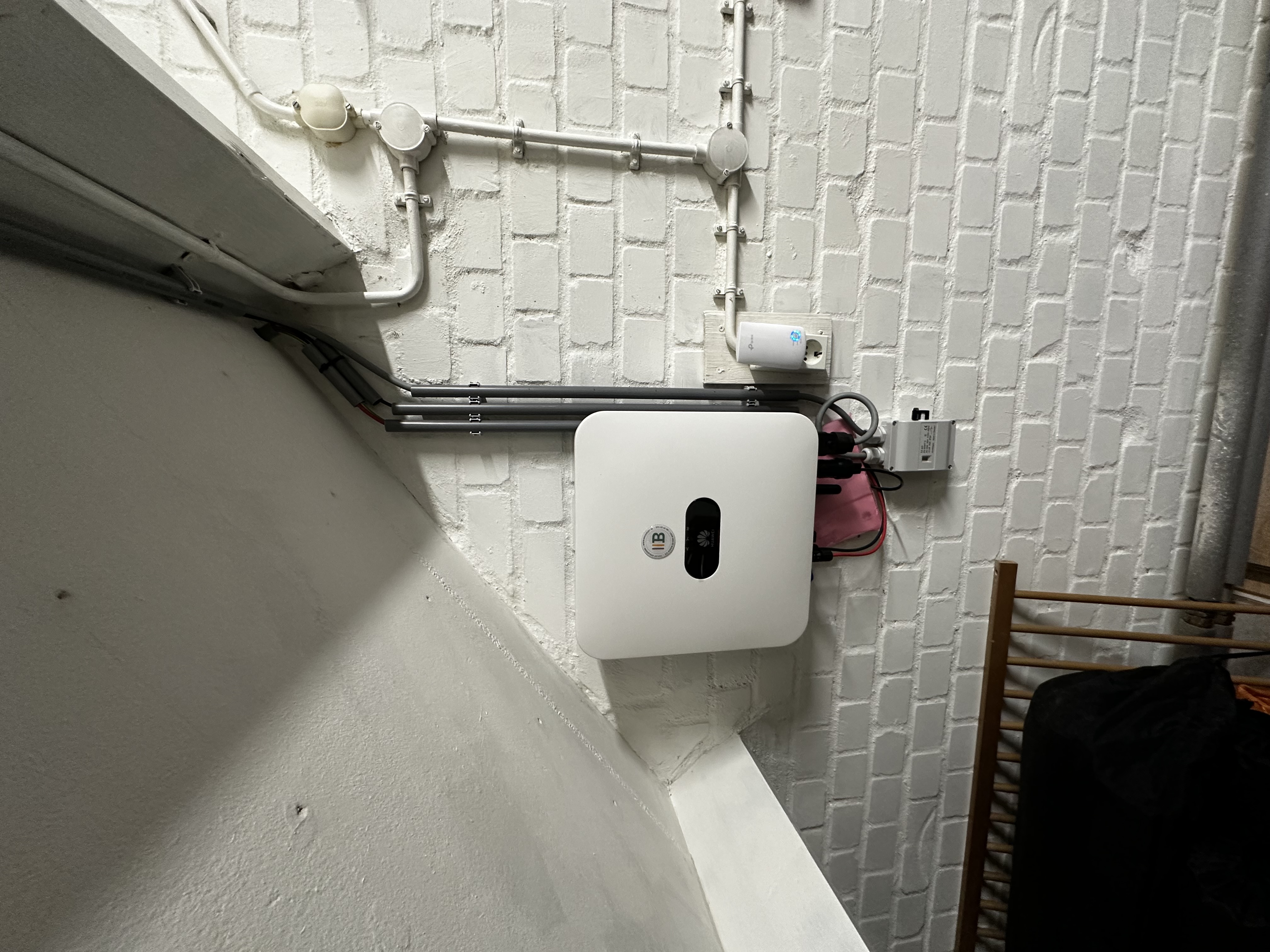 Installatie van een omvormer voor zonnepanelen, zichtbaar met bekabeling. Geplaatst aan een muur in een interieur.
