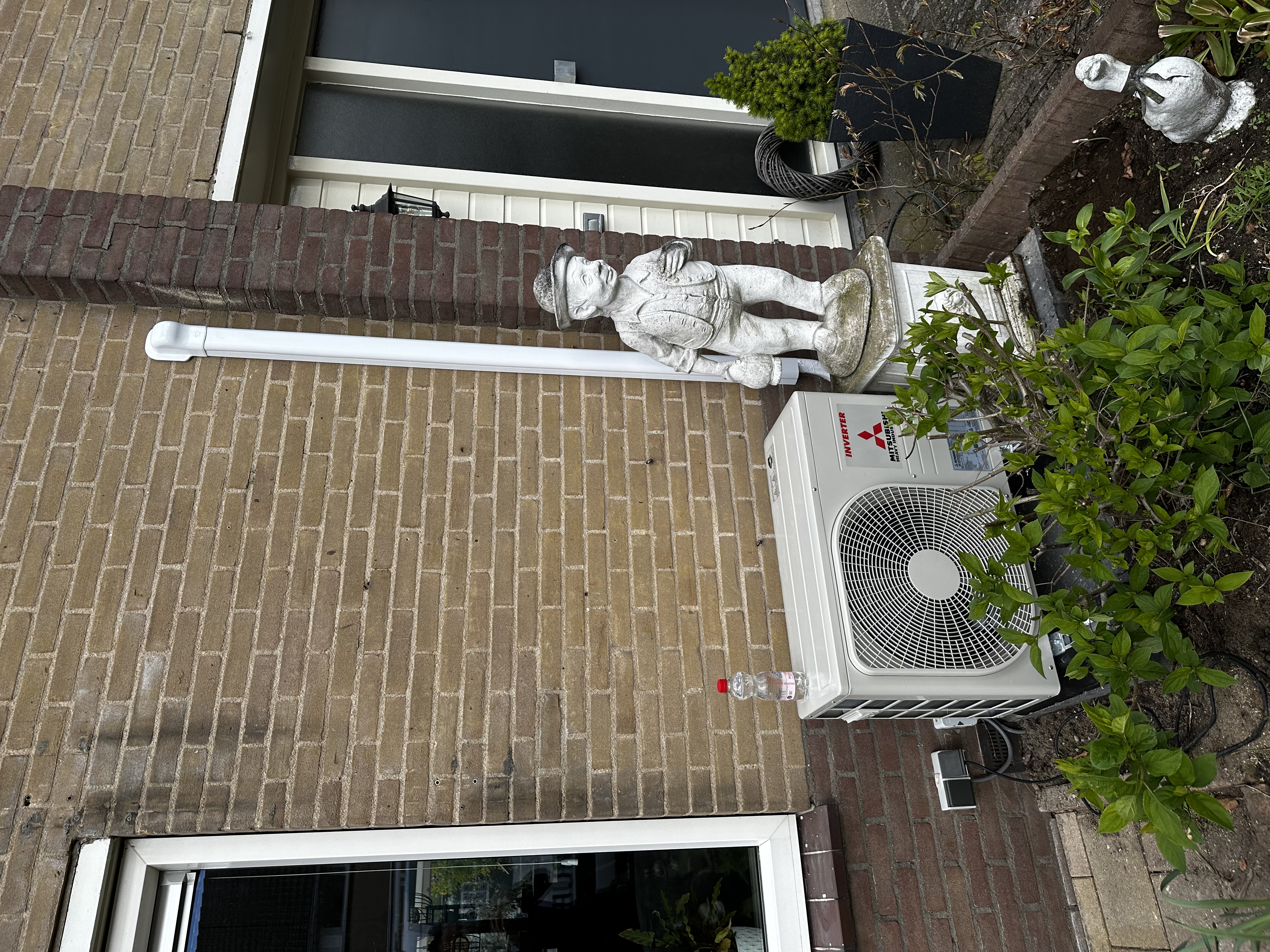 Een wandunit voor airconditioning is geïnstalleerd buiten, naast een huis. De unit heeft een inverter technologie.