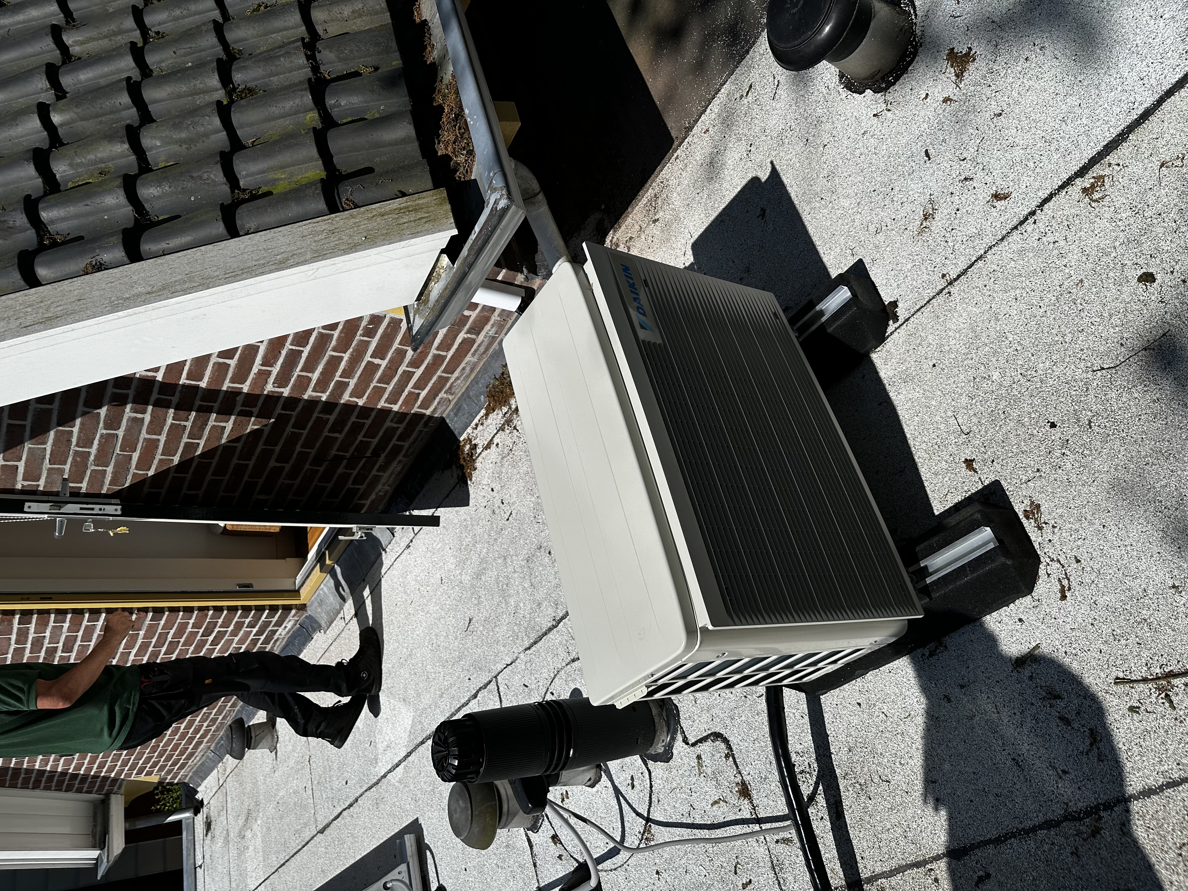 Een airco-unit wordt geïnstalleerd op een plat dak met toegang tot een deur.
