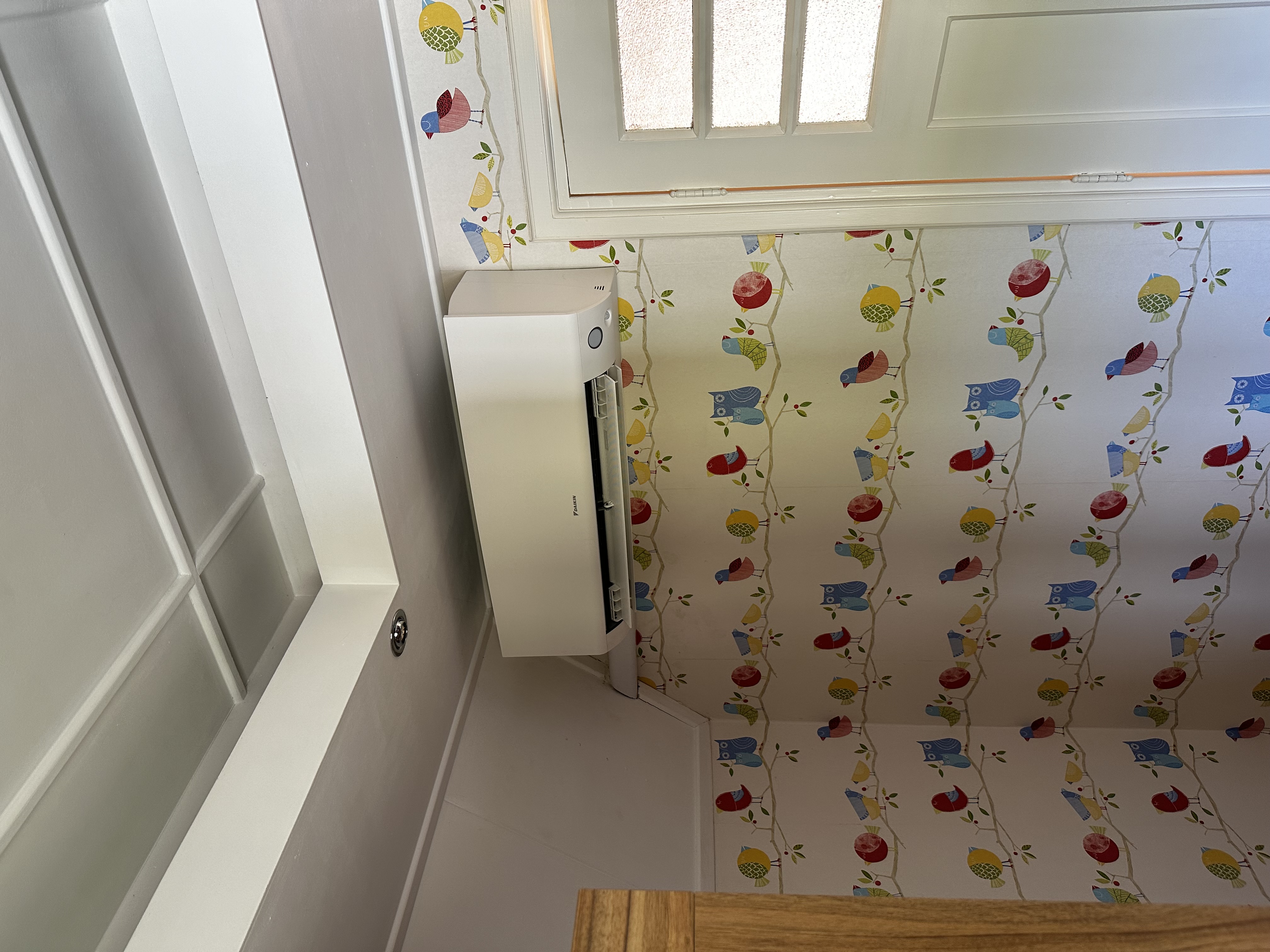 De afbeelding toont een geïnstalleerde airconditioningseenheid aan de muur, met een kleurrijke achtergrond van vogels en bladeren.