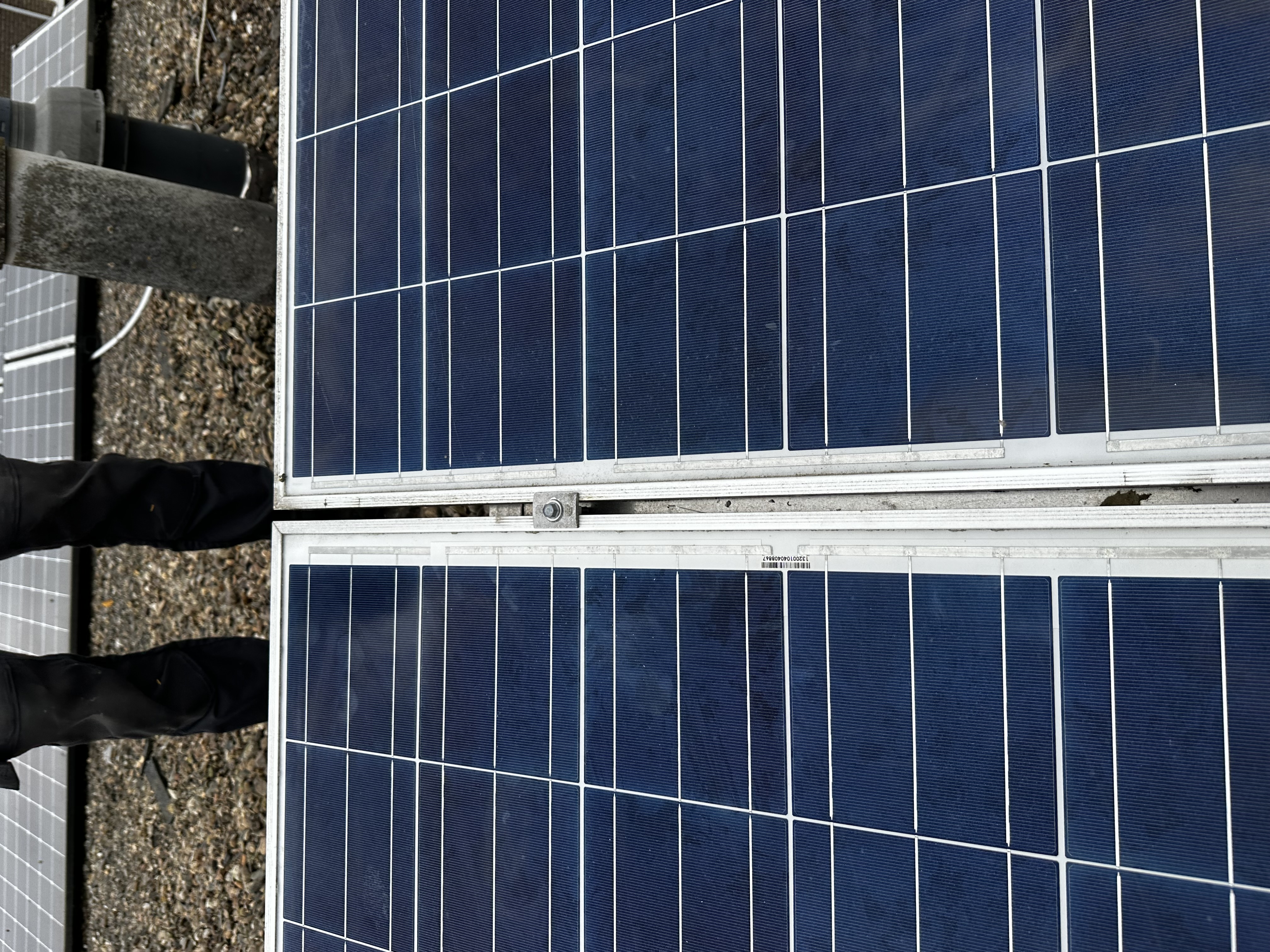 Detail van een zonnepaneleninstallatie, gericht op de verbinding tussen panelen op een grindbed.