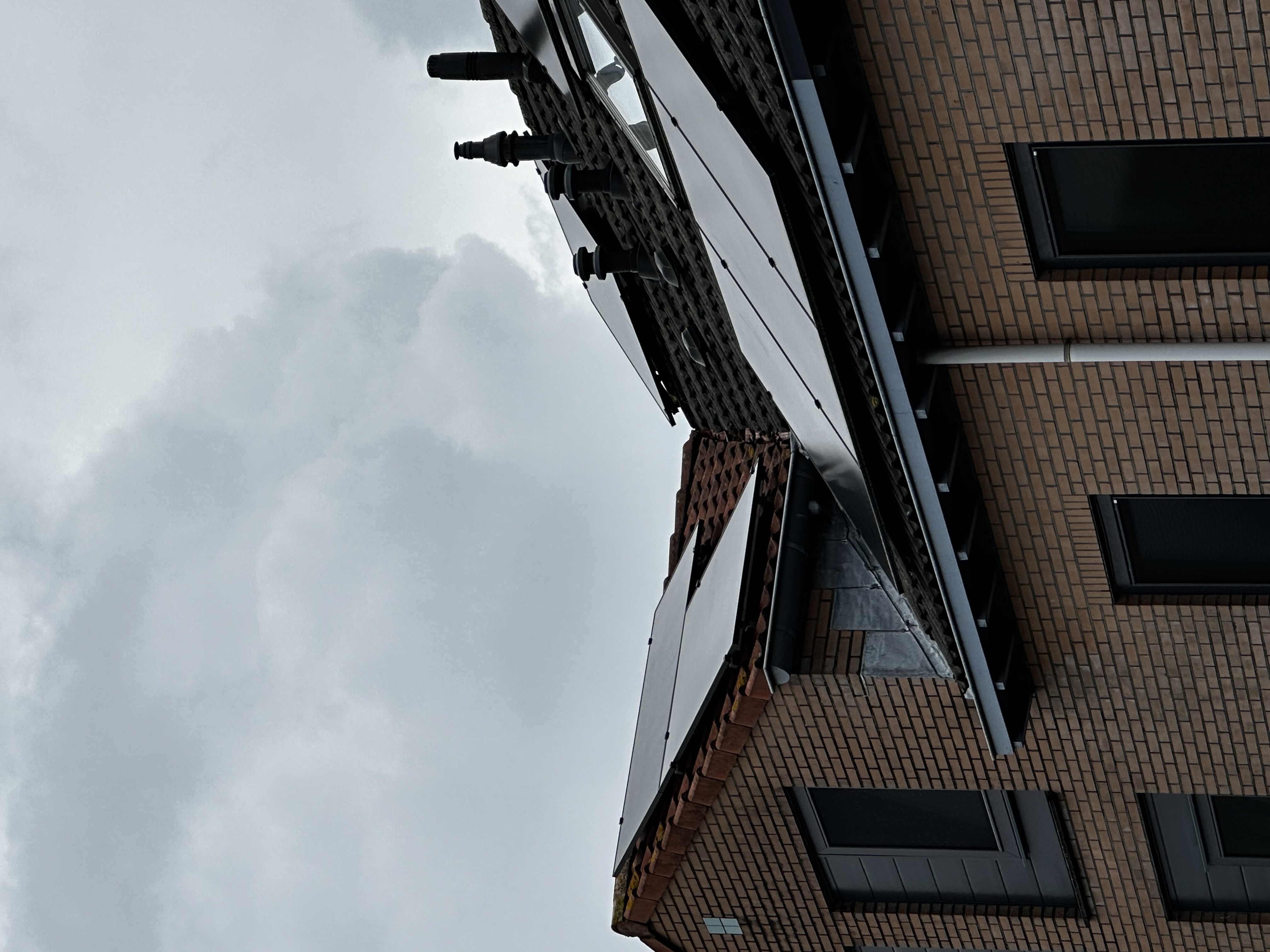 De afbeelding toont zonnepanelen geïnstalleerd op een hellend dak van een woning, met een grijze lucht op de achtergrond.