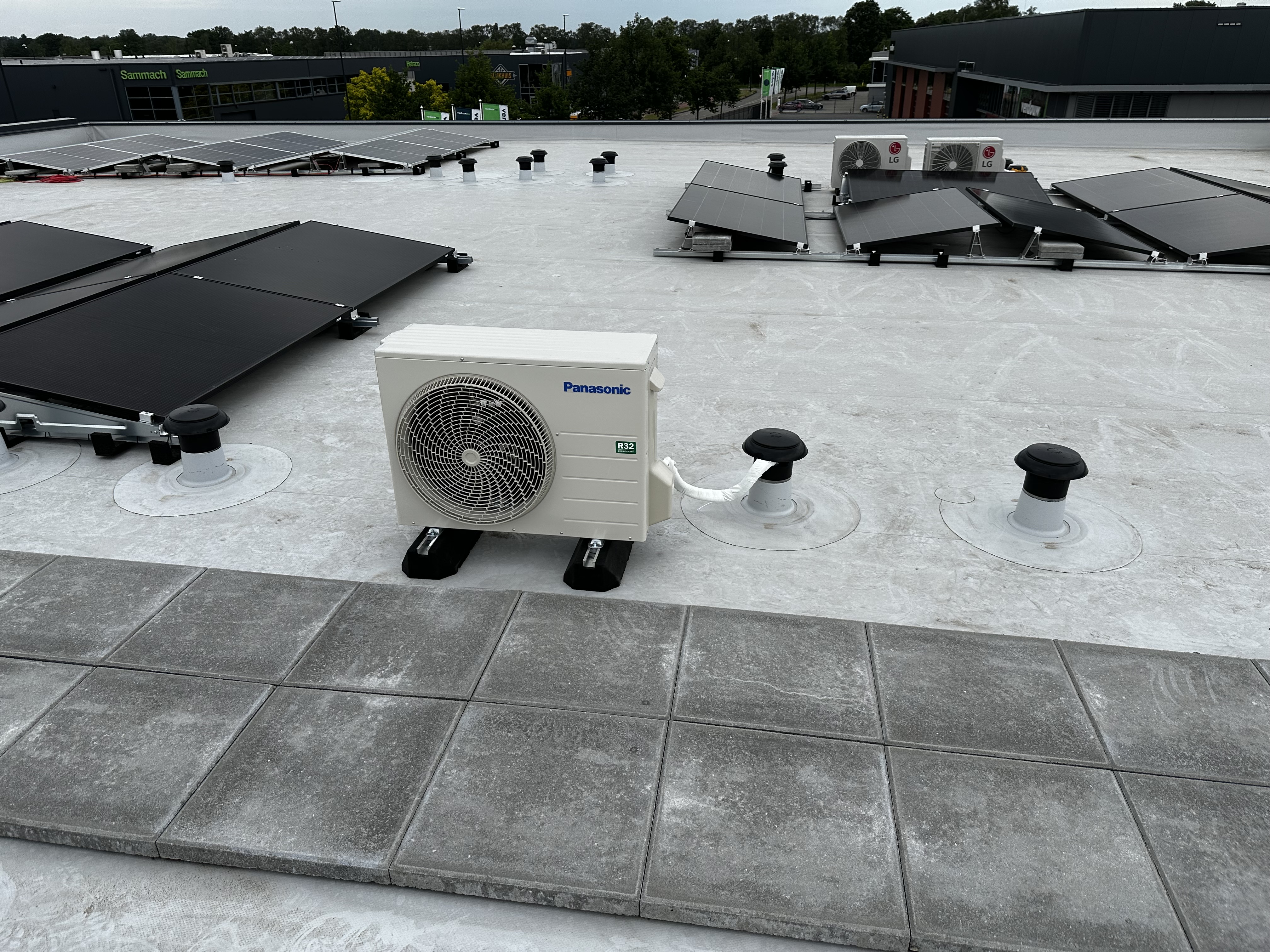 Een airconditioningseenheid op het dak, naast zonnepanelen, die koelcomfort biedt voor het gebouw.