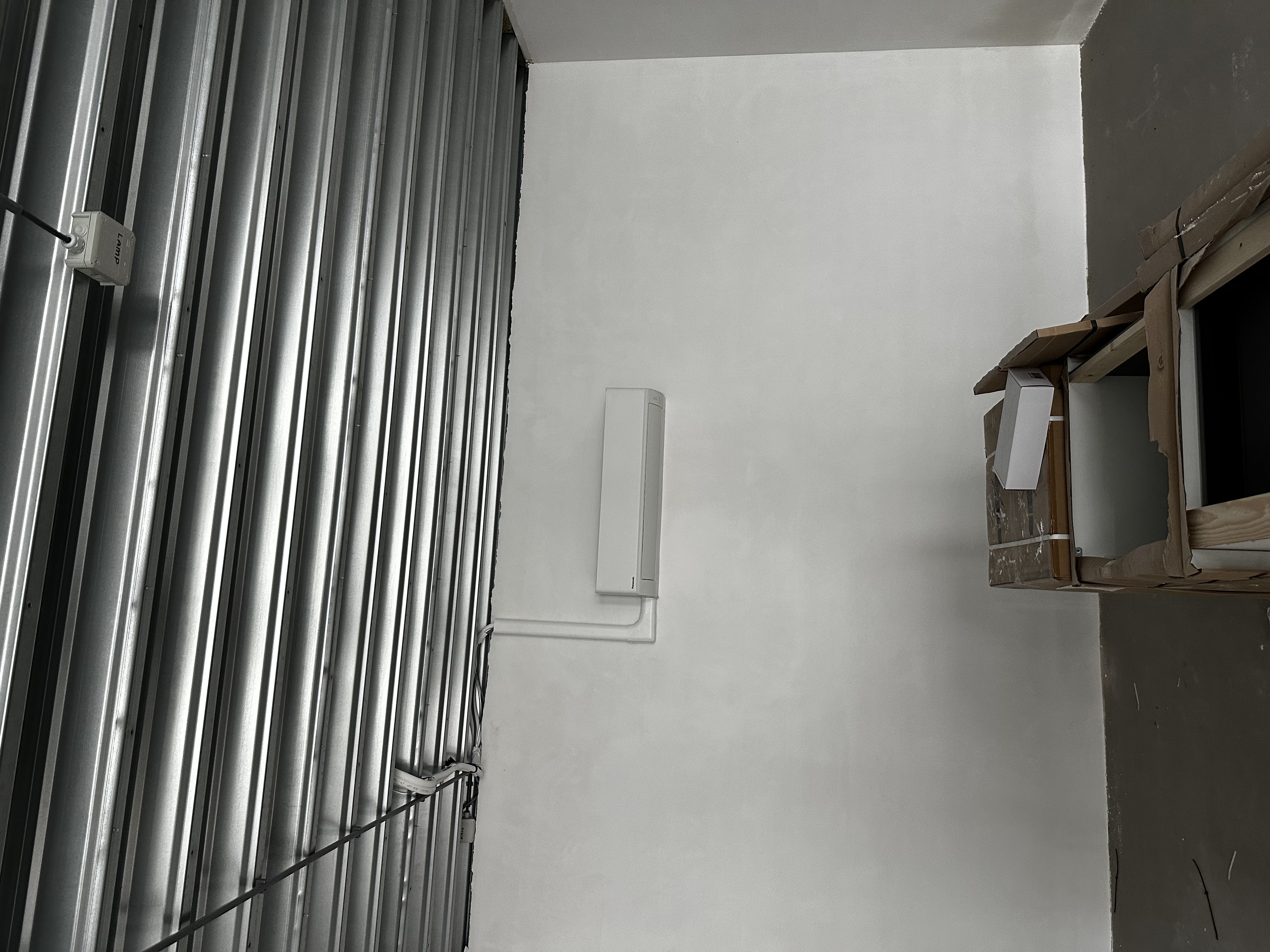 Een recent geïnstalleerde airconditioningseenheid aan de muur in een onafgebouwde ruimte.