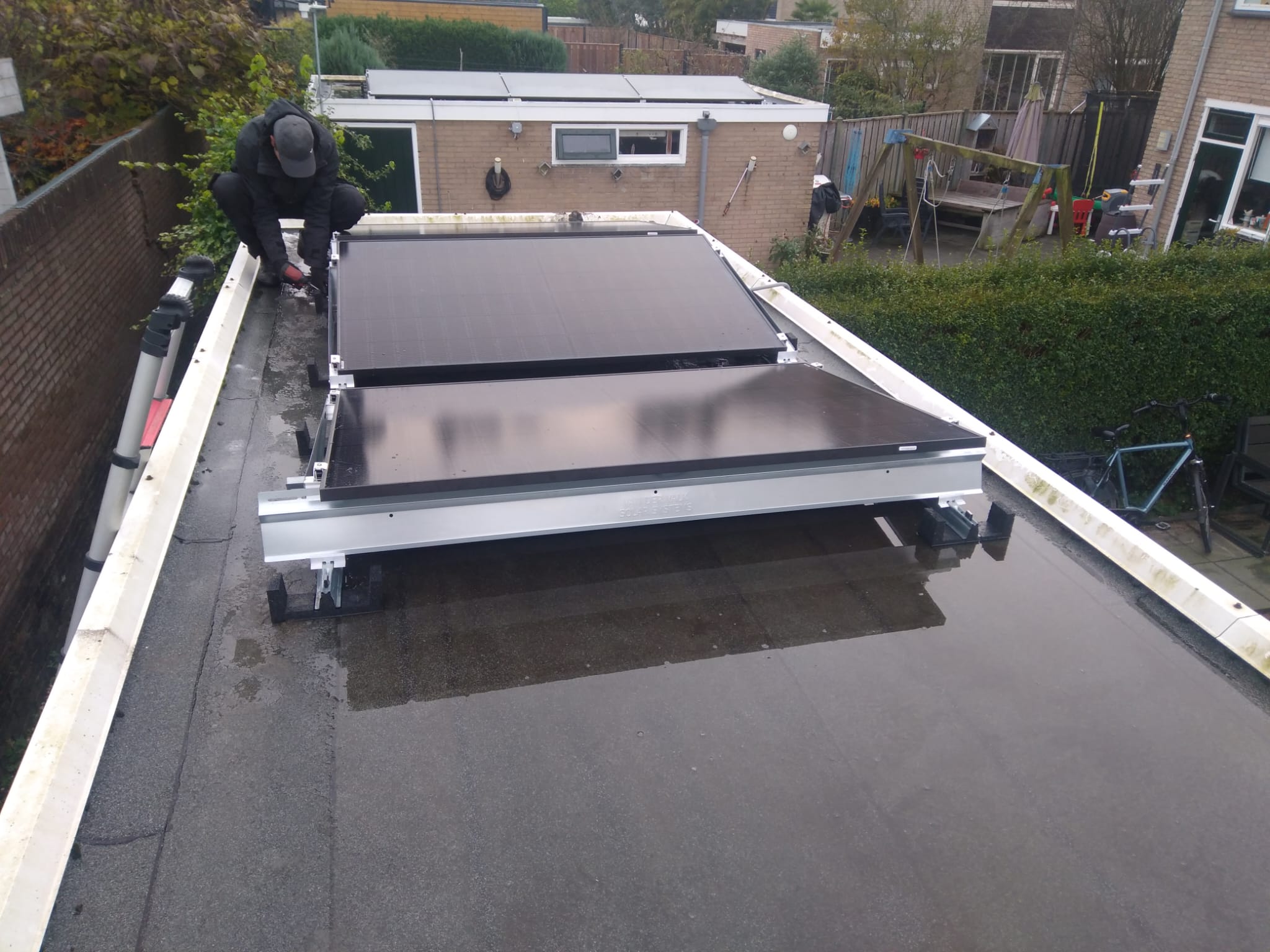 Twee zonnepanelen worden geïnstalleerd op een plat dak, met een technicus die de bevestiging uitvoert.