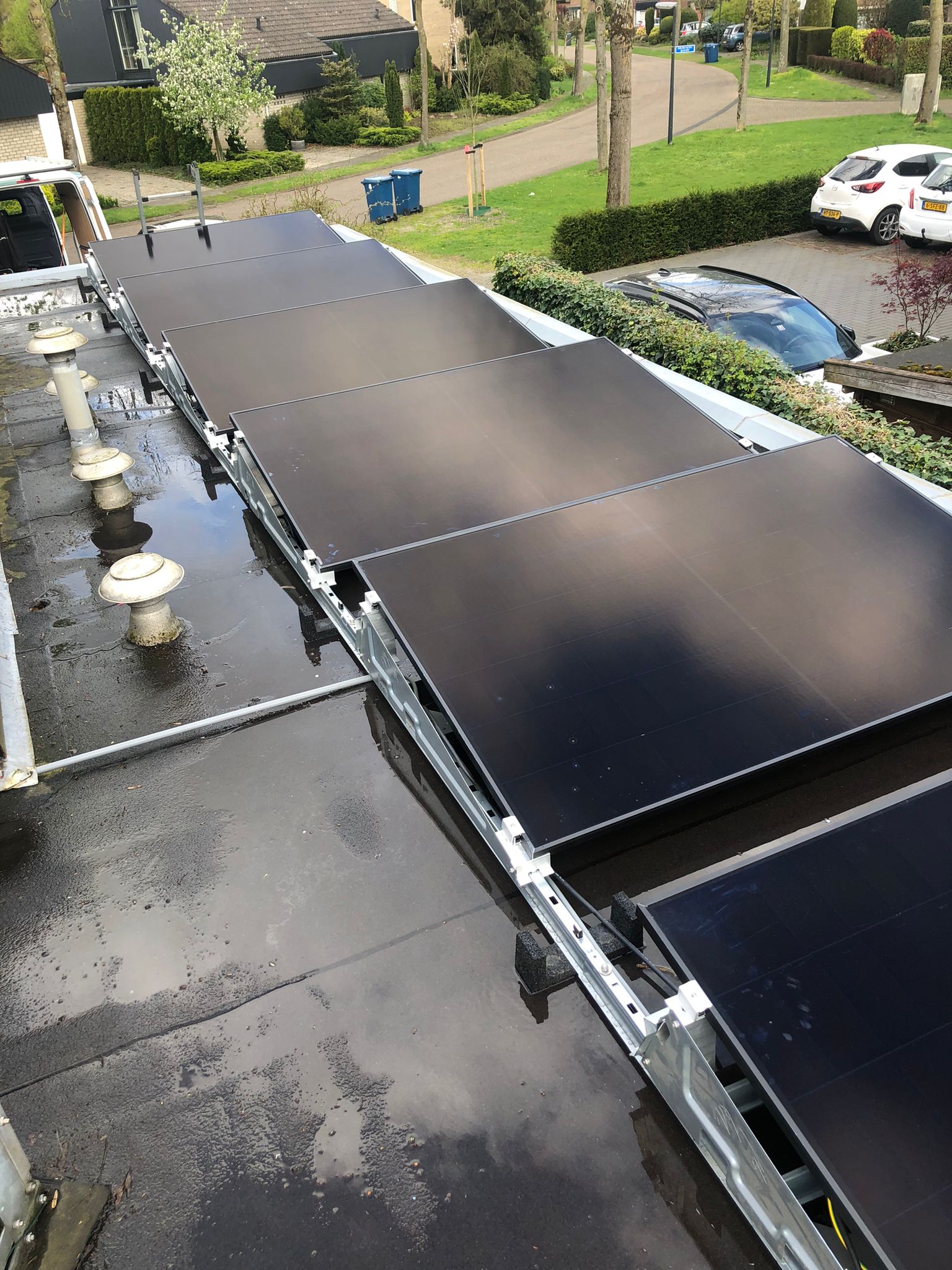 Een reeks zonnepanelen zijn geïnstalleerd op een plat dak, zichtbaar met bevestigingsmateriaal en waterreflecties op het oppervlak.