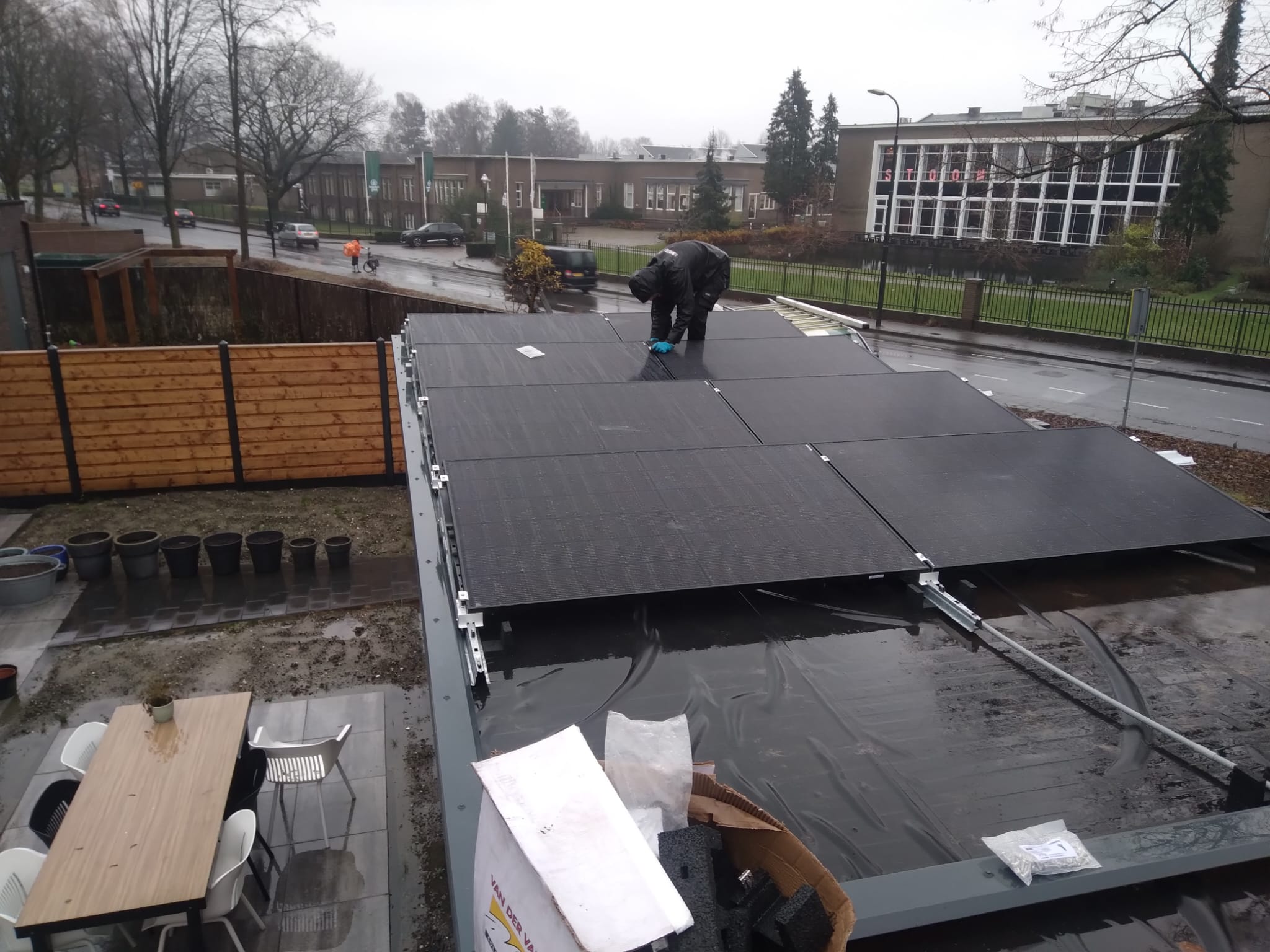 De foto toont een installatie van zonnepanelen op een dak, met een technicus die de panelen aanbrengt.