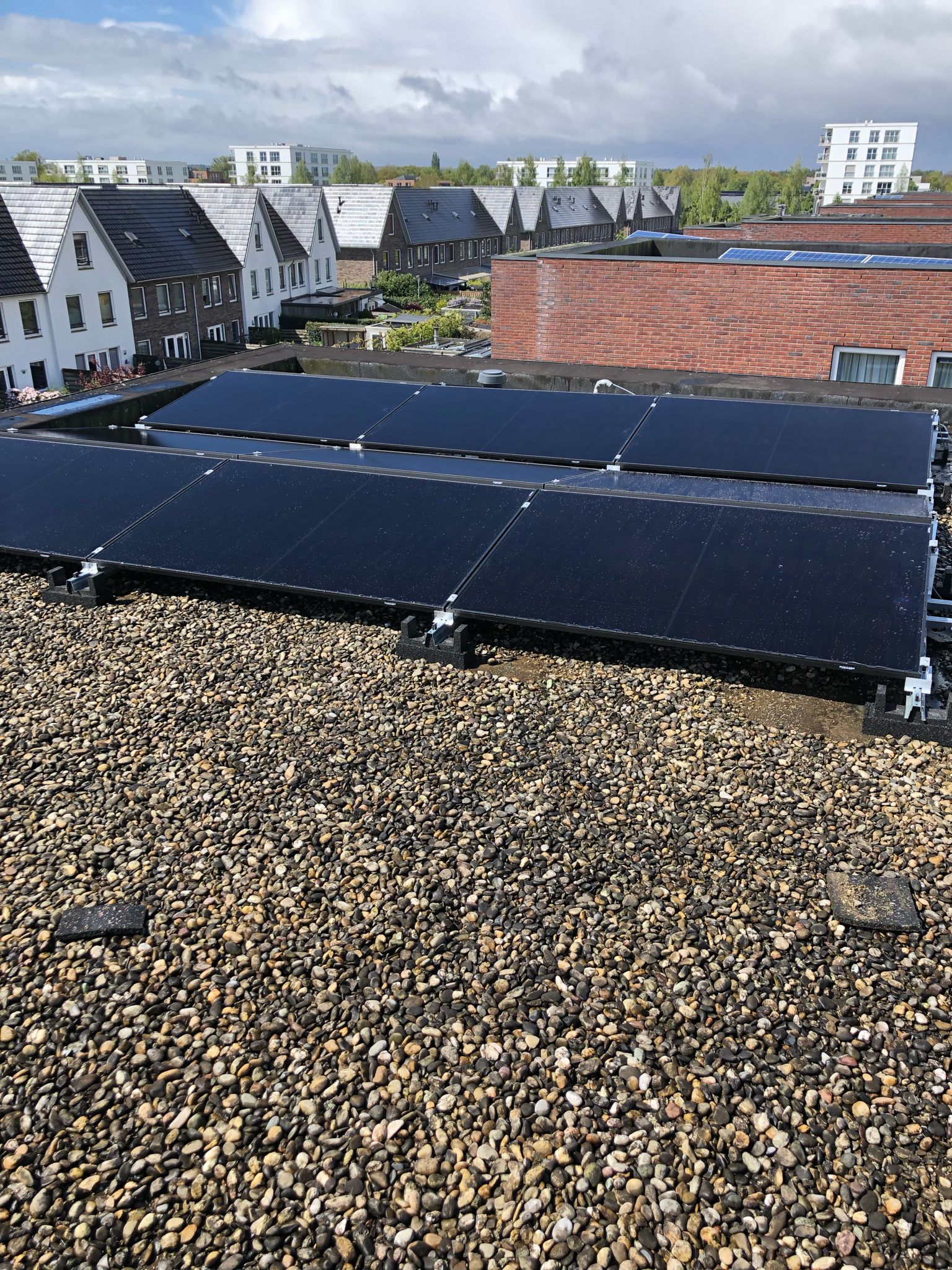 Zonnepanelen zijn geïnstalleerd op een plat dak van een woning, met een uitzicht op de omliggende huizen.