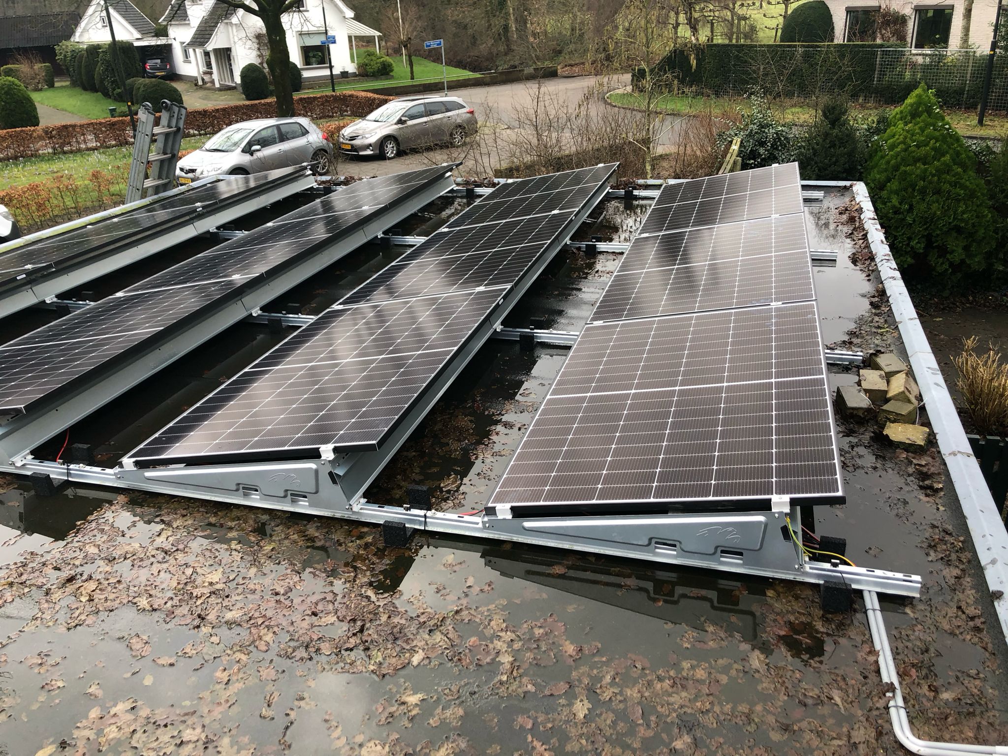 De afbeelding toont een installatie van zonnepanelen op een vlakke ondergrond, mogelijk een dak, met loeiende bladeren en water rondom.